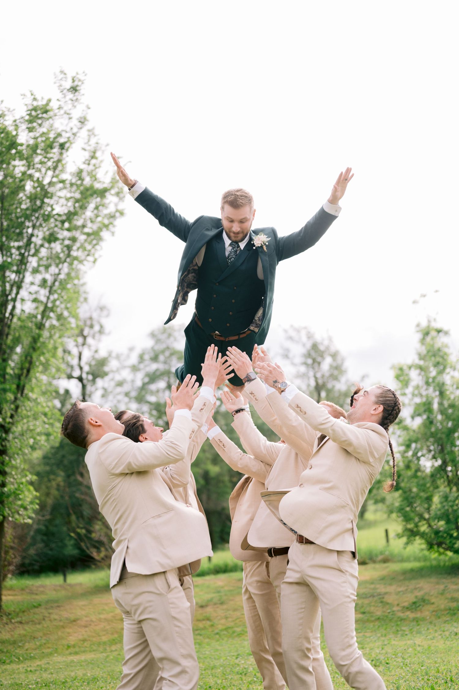 Groomsmen in khaki suits toss the groom in the air during a fun wedding photo.