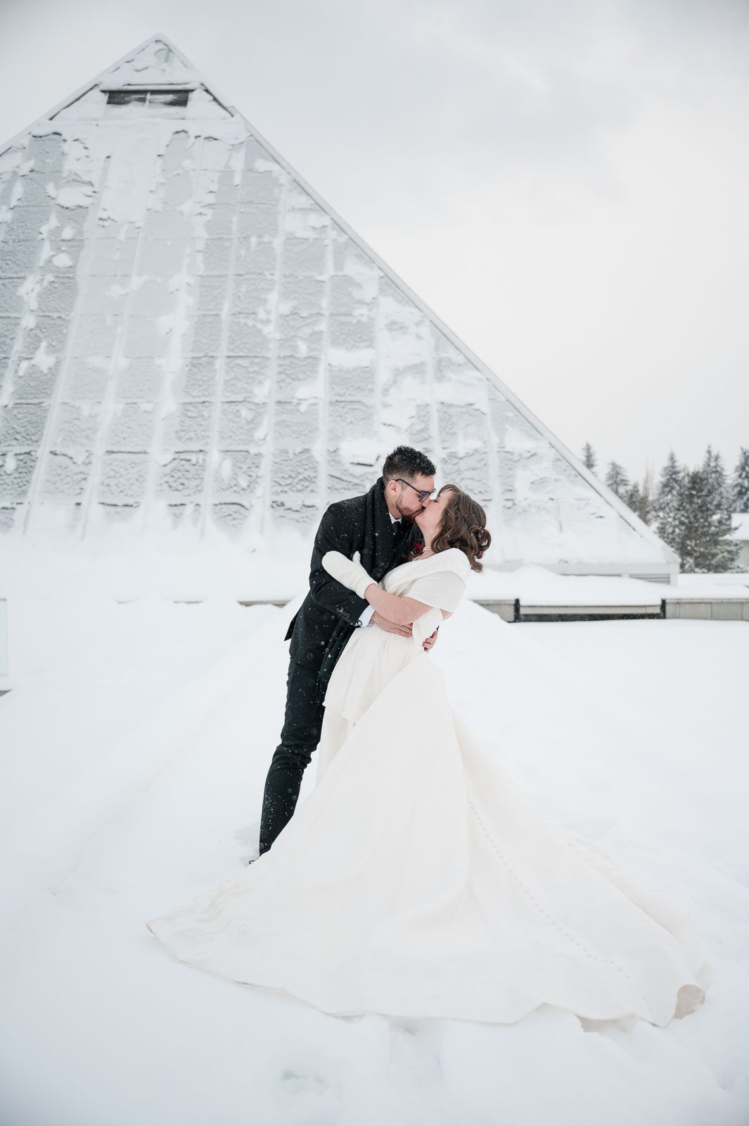 Winter wedding photos featuring a couple embracing in front of a snow-covered geometric structure.