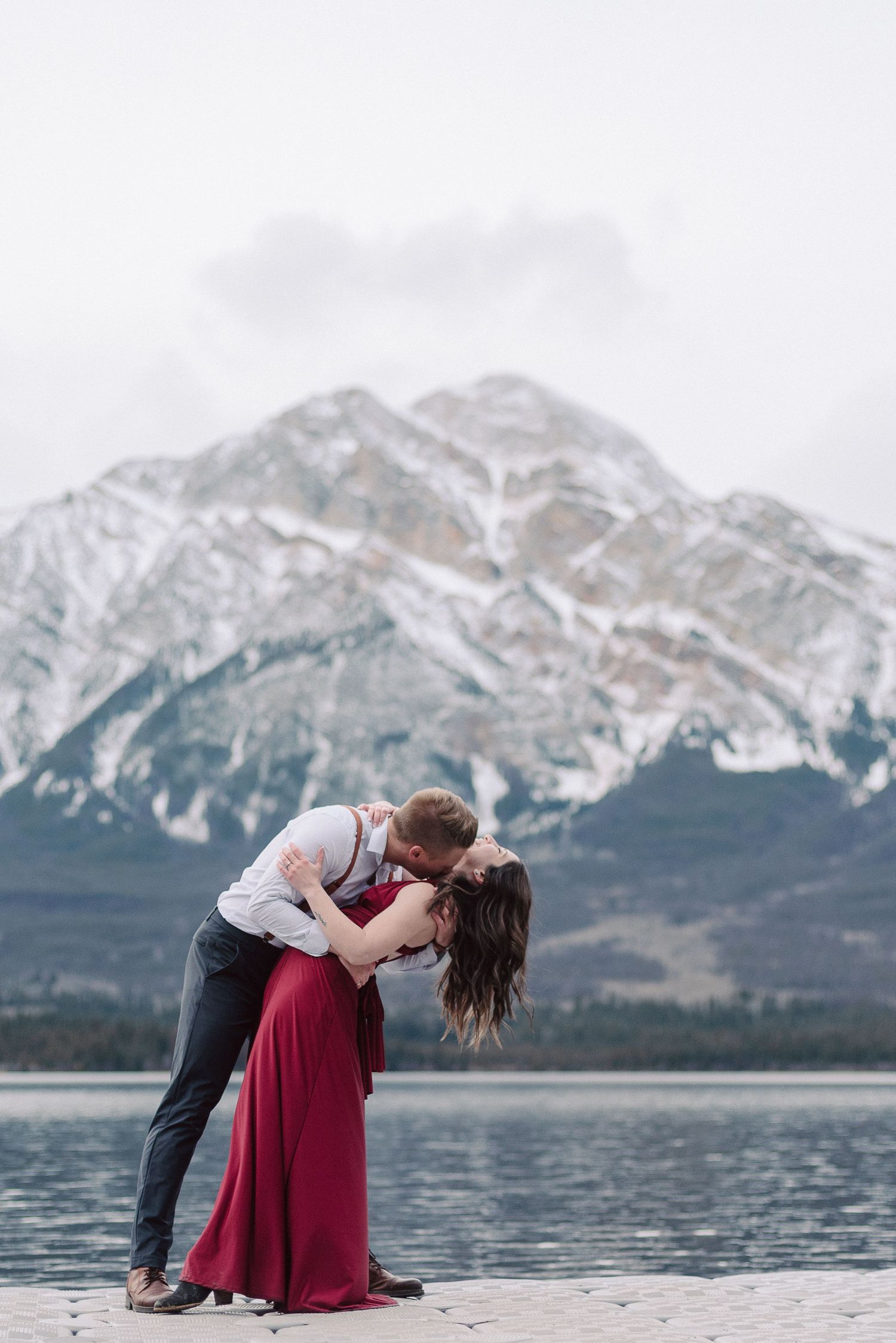 Couple in romantic pose with dramatic mountain landscape and lake backdrop.