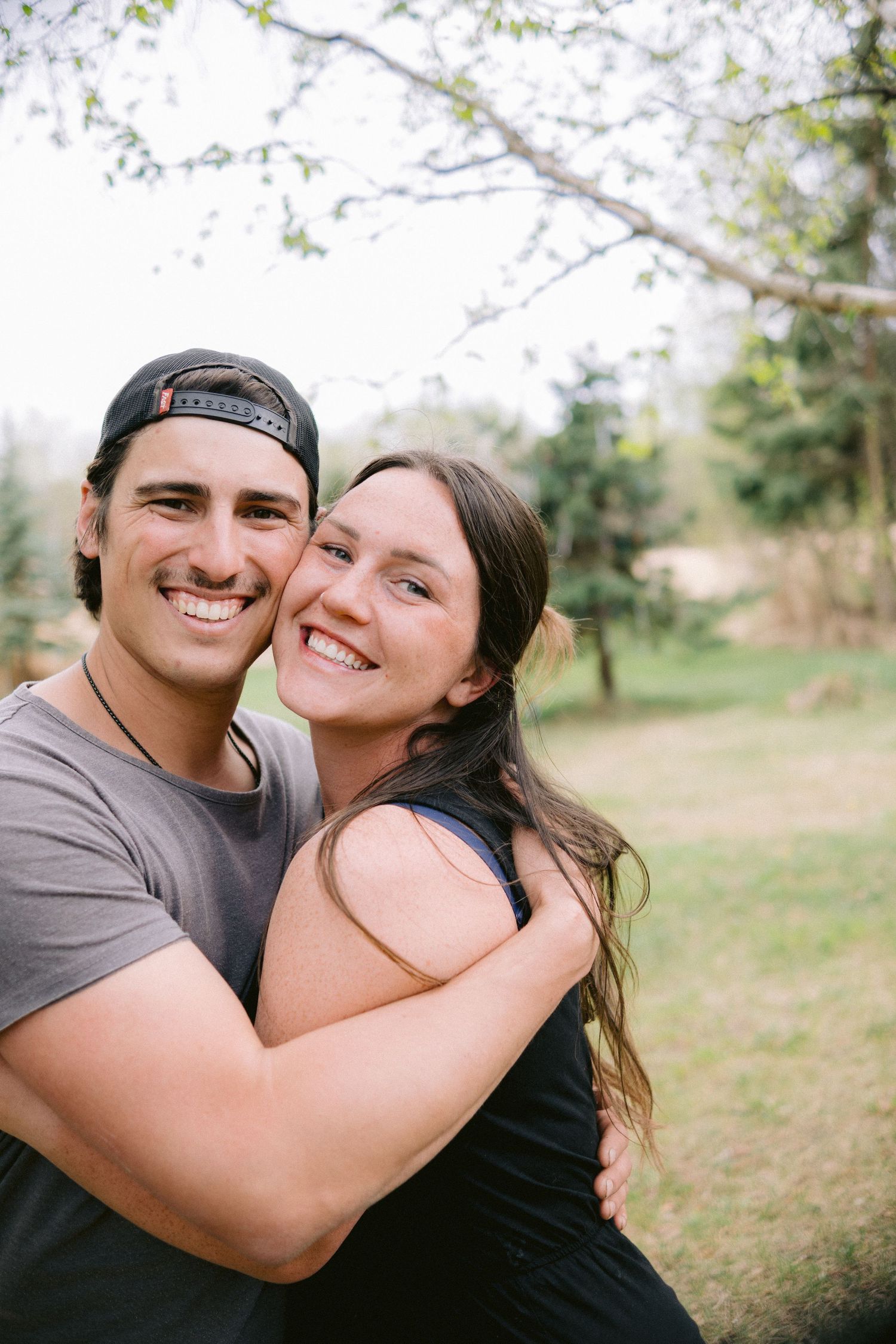 Affectionate couple sharing intimate moments outdoors under blooming spring trees.