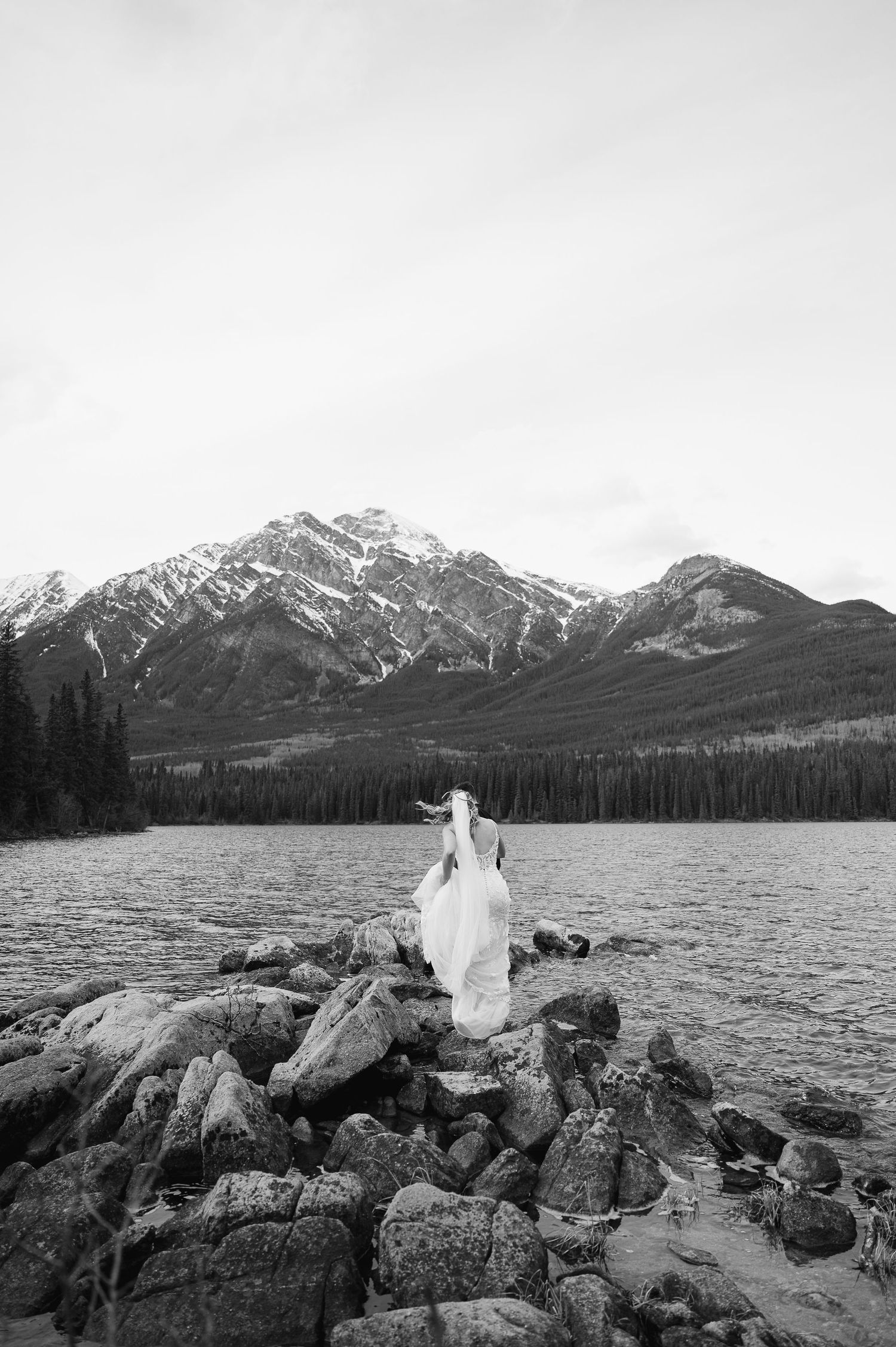 A dramatic black and white wedding photoshoot with mountain peaks and a lake in Jasper National Park.