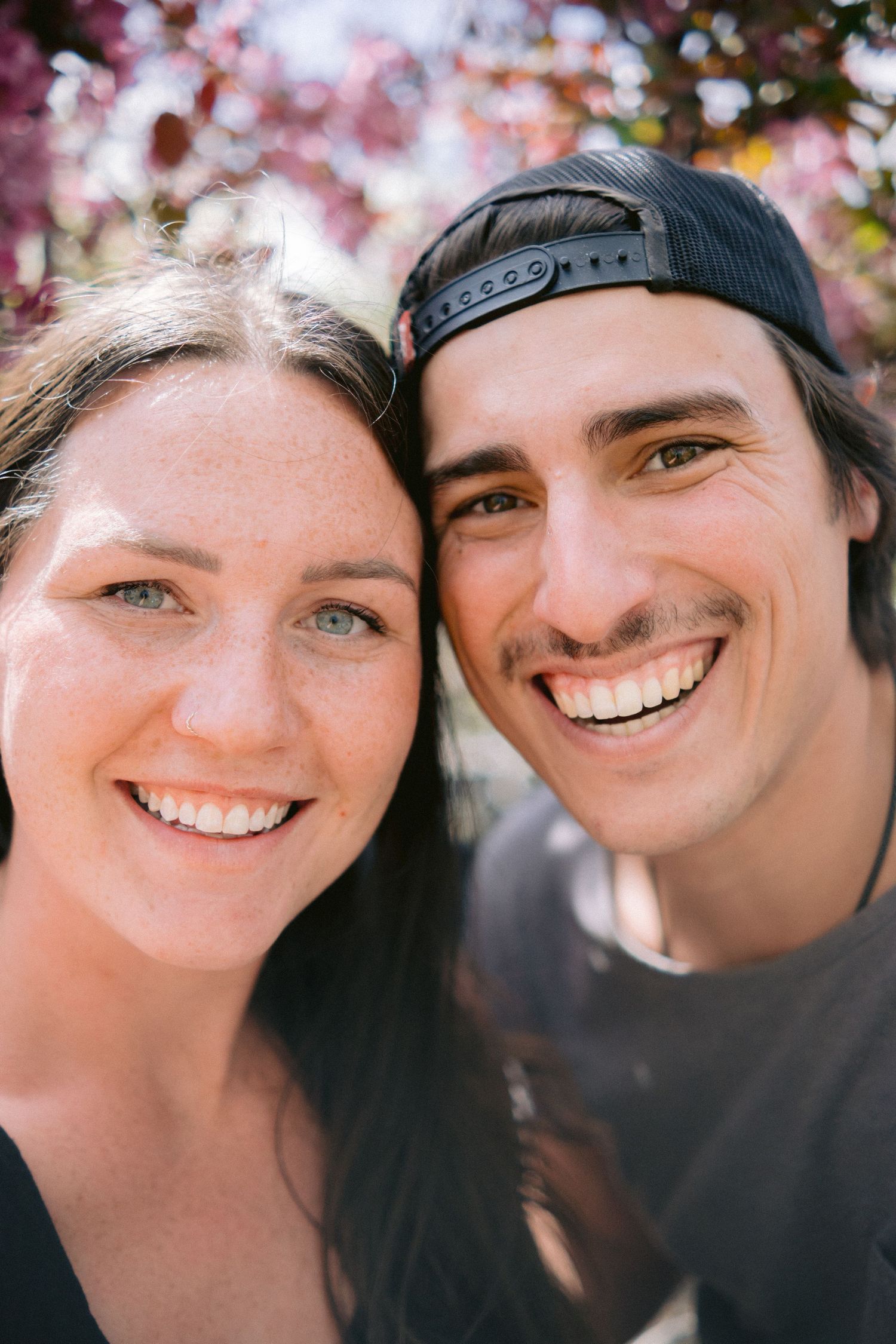 Close up portraits of a smiling couple against pink cherry blossoms in spring.