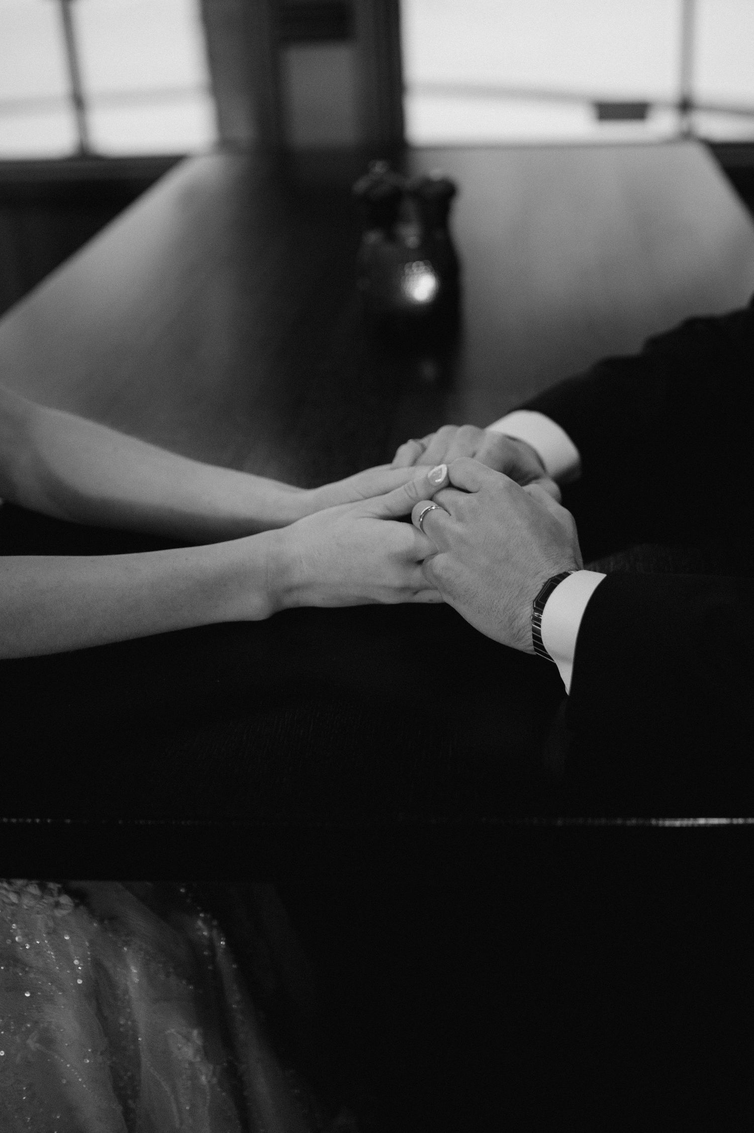 Close-up black and white photo of hands with wedding rings touching across a table.