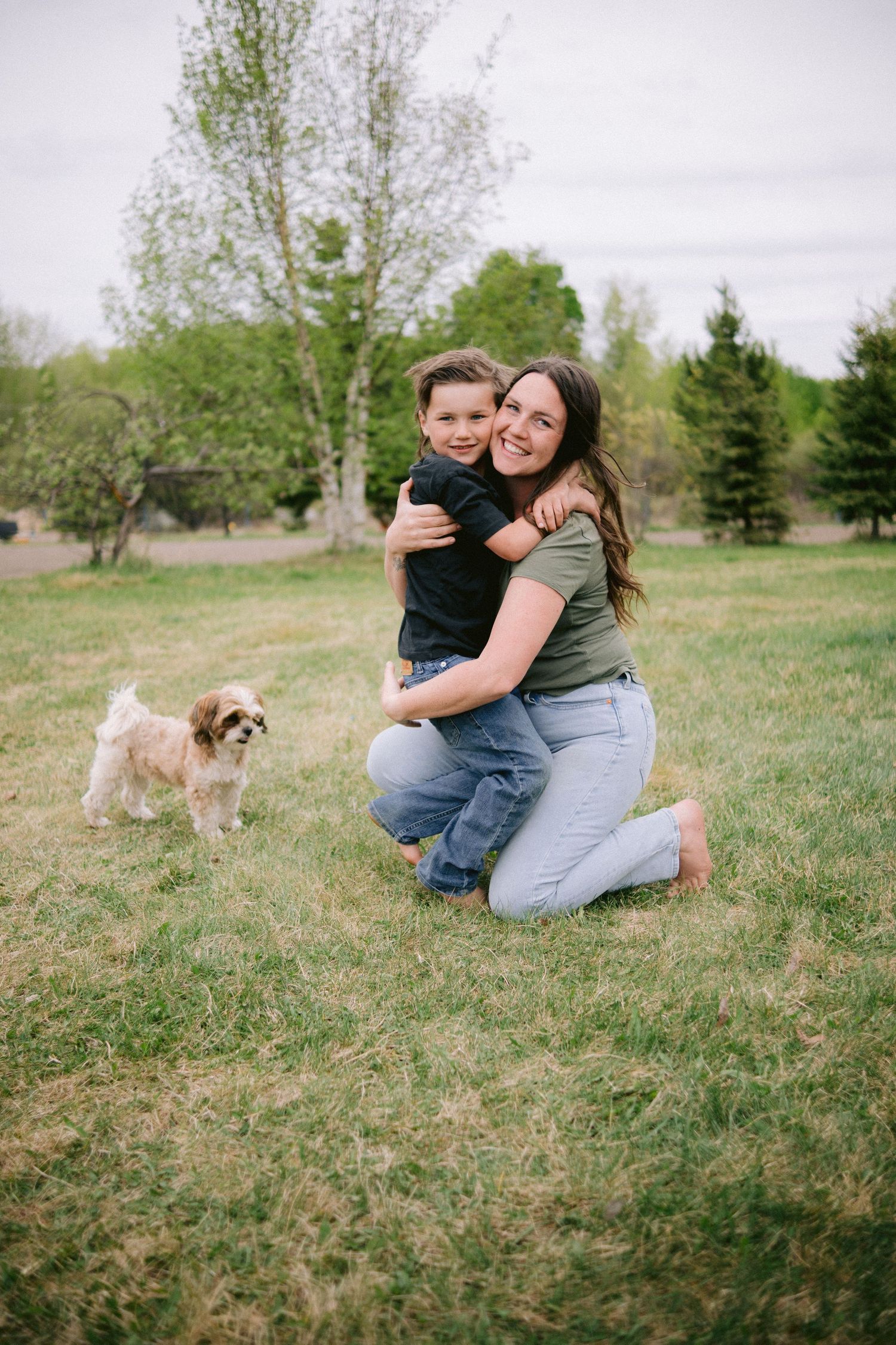 Playful outdoor family portraits in a grassy field with a dog visible in the background.
