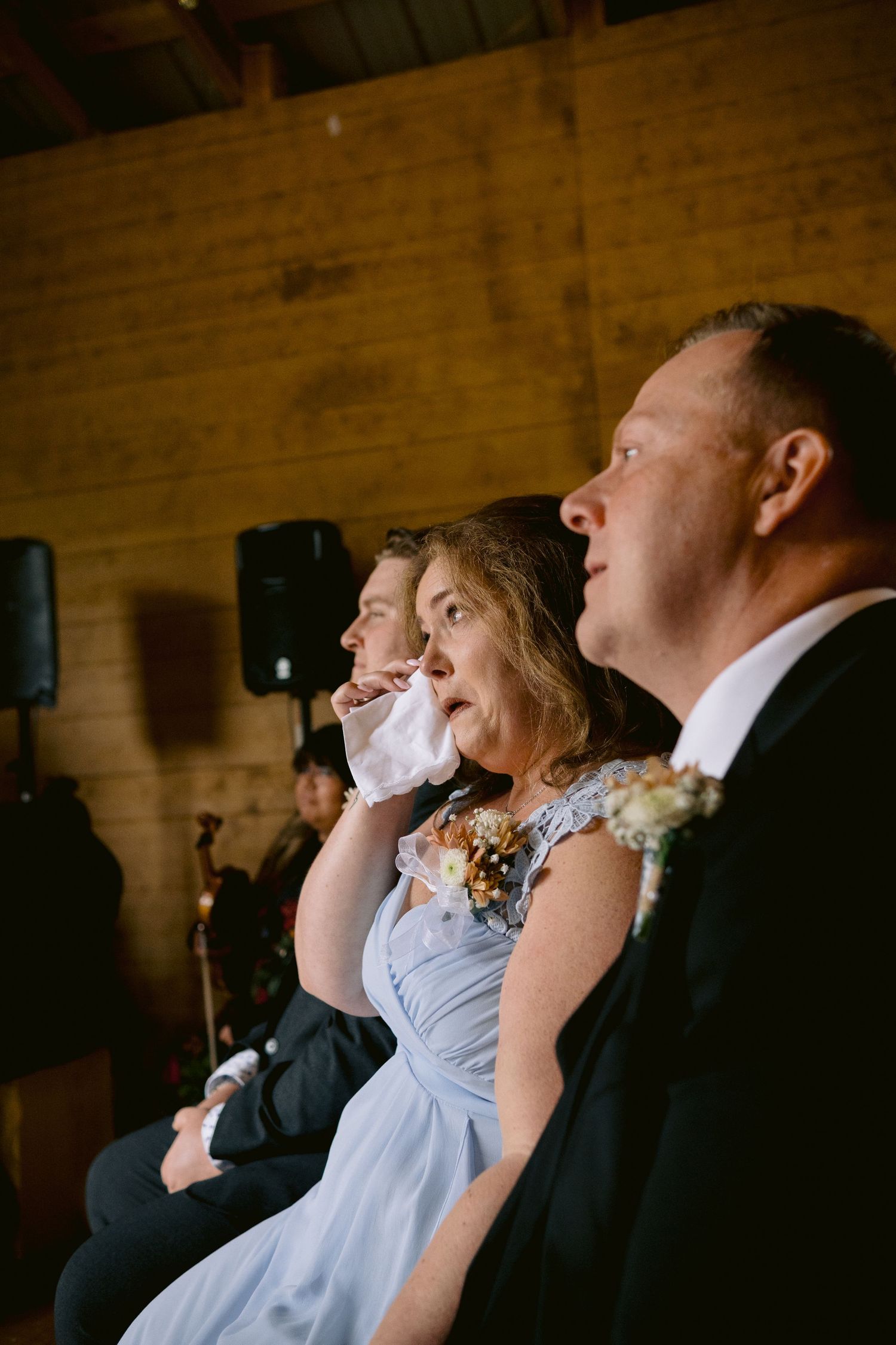 Wedding guests react emotionally during a ceremony in a rustic wooden venue.
