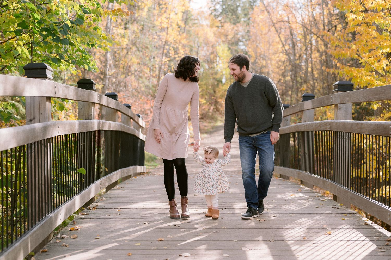 Family walking together on wooden bridge surrounded by autumn foliage.