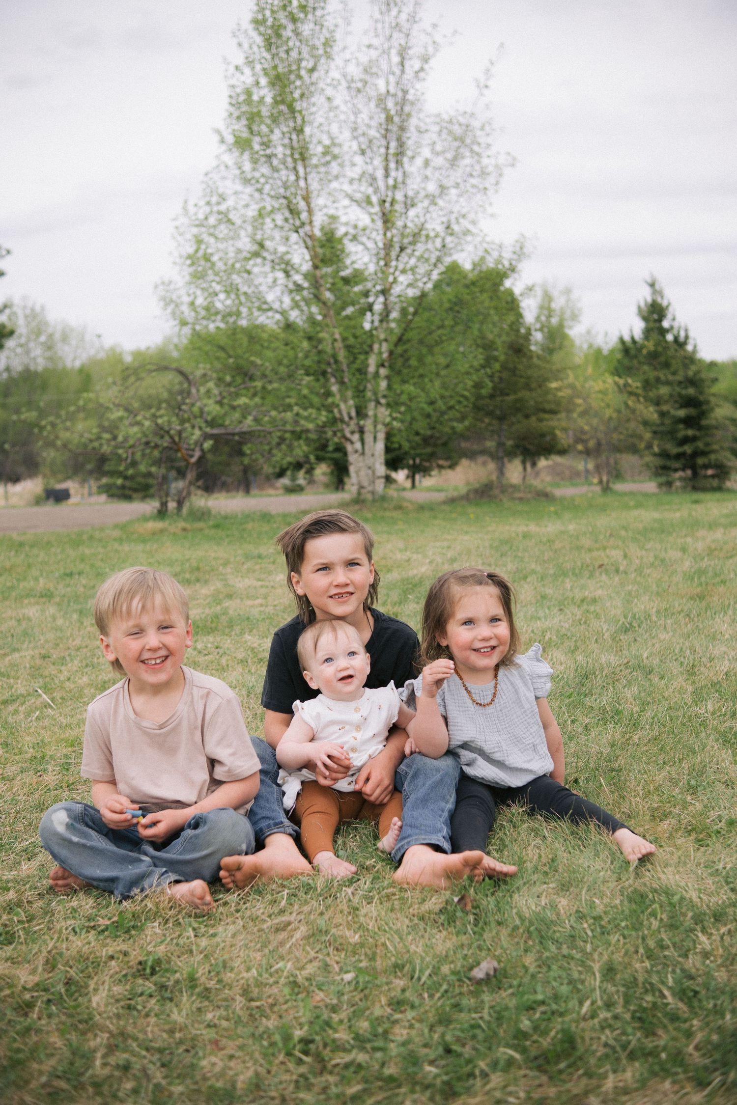 Children sitting together and smiling on grass in a natural outdoor setting.