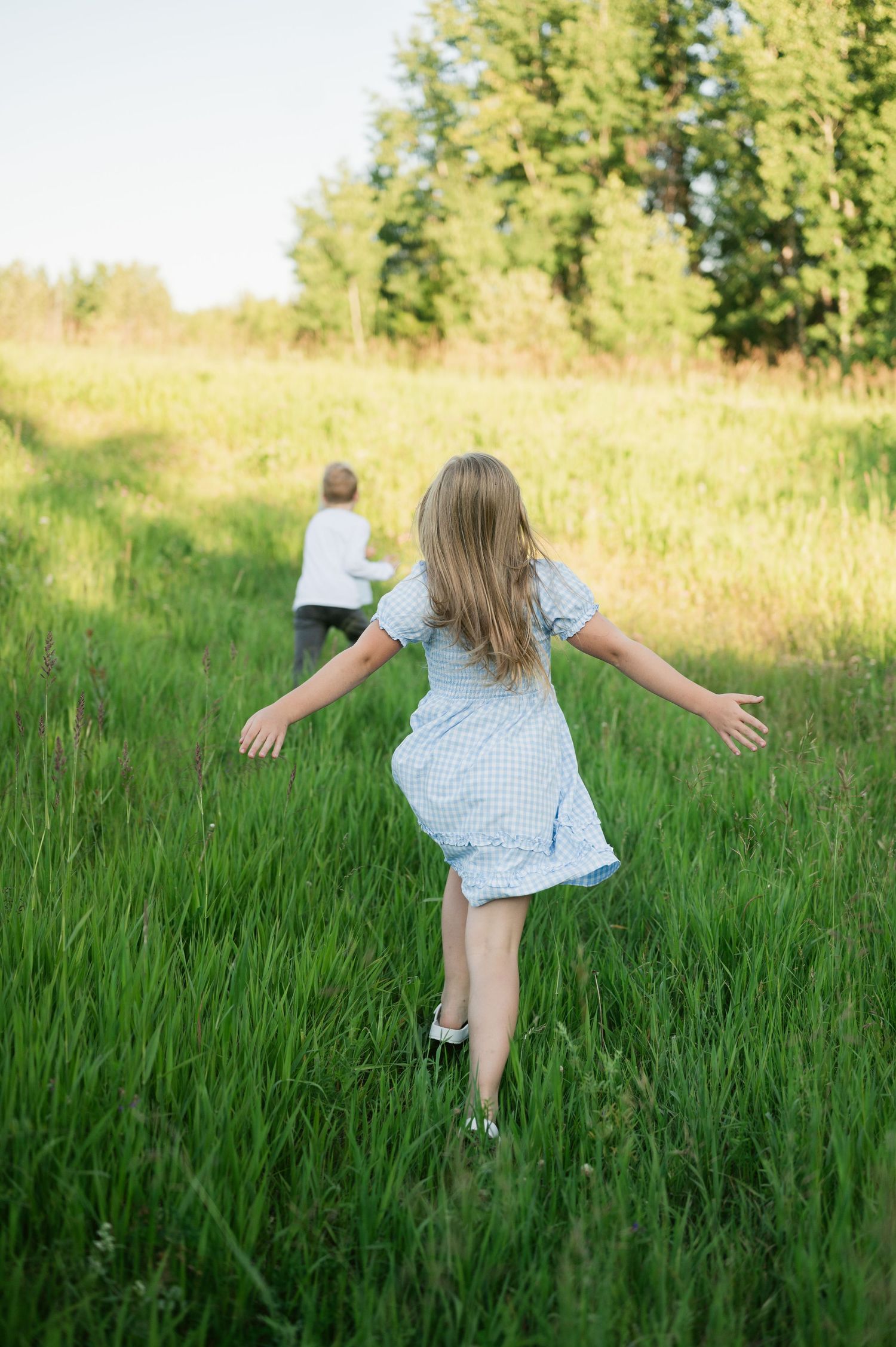 Young child in a blue dress frolics joyfully through tall green grass in a sunny summer meadow.