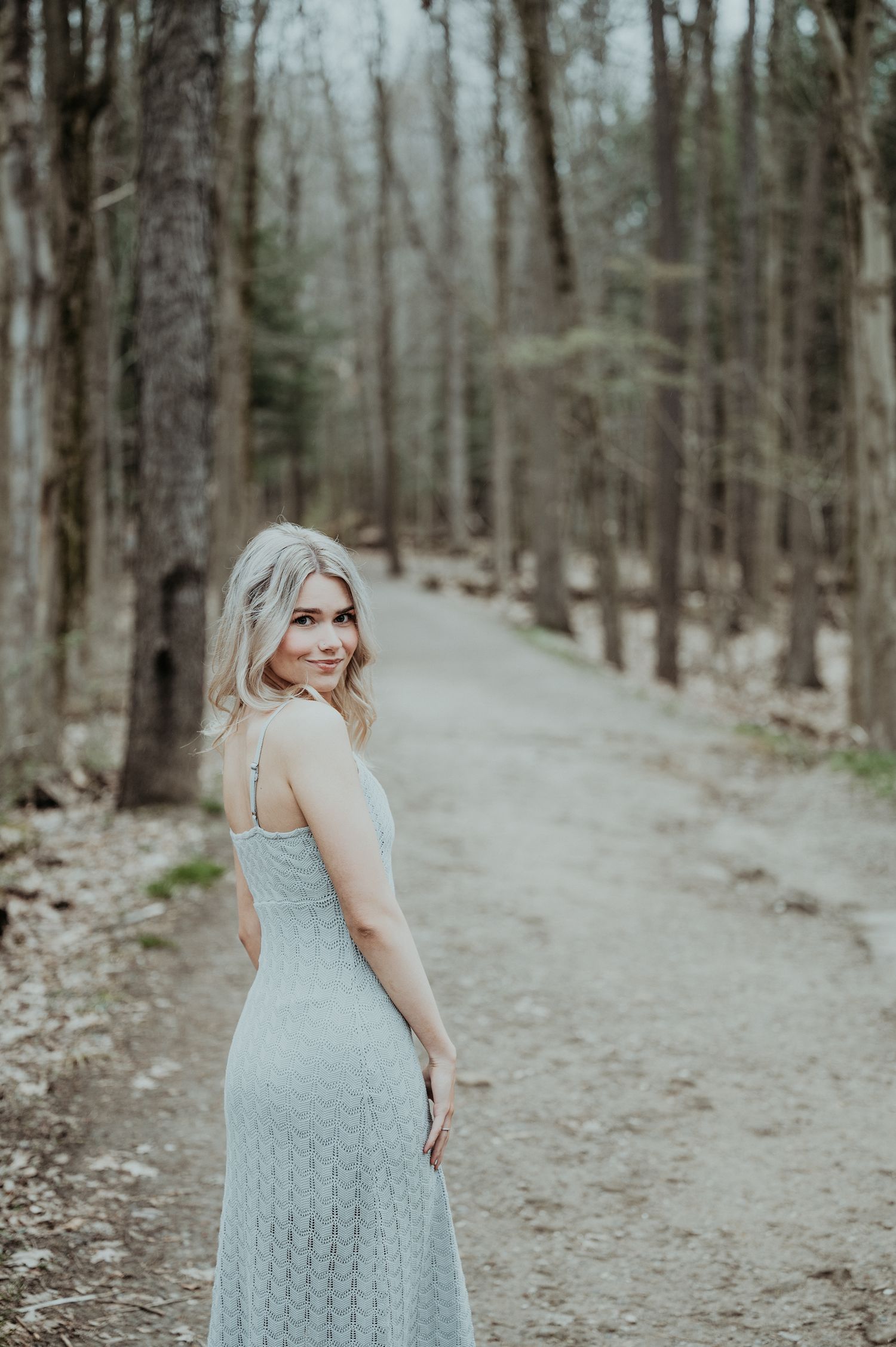 Someone in a light blue lace dress walks along a winding forest path through bare winter trees.
