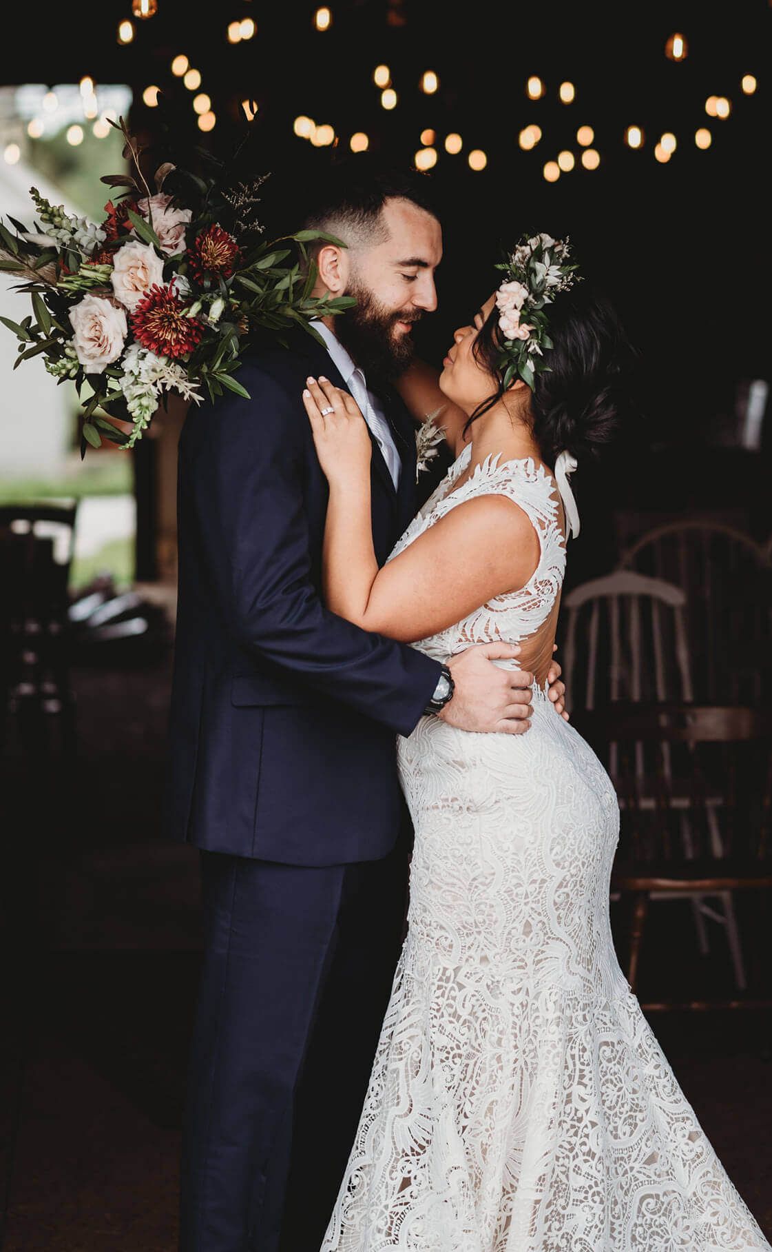 A romantic wedding moment with a couple embracing under warm string lights surrounded by elegant floral bouquets.