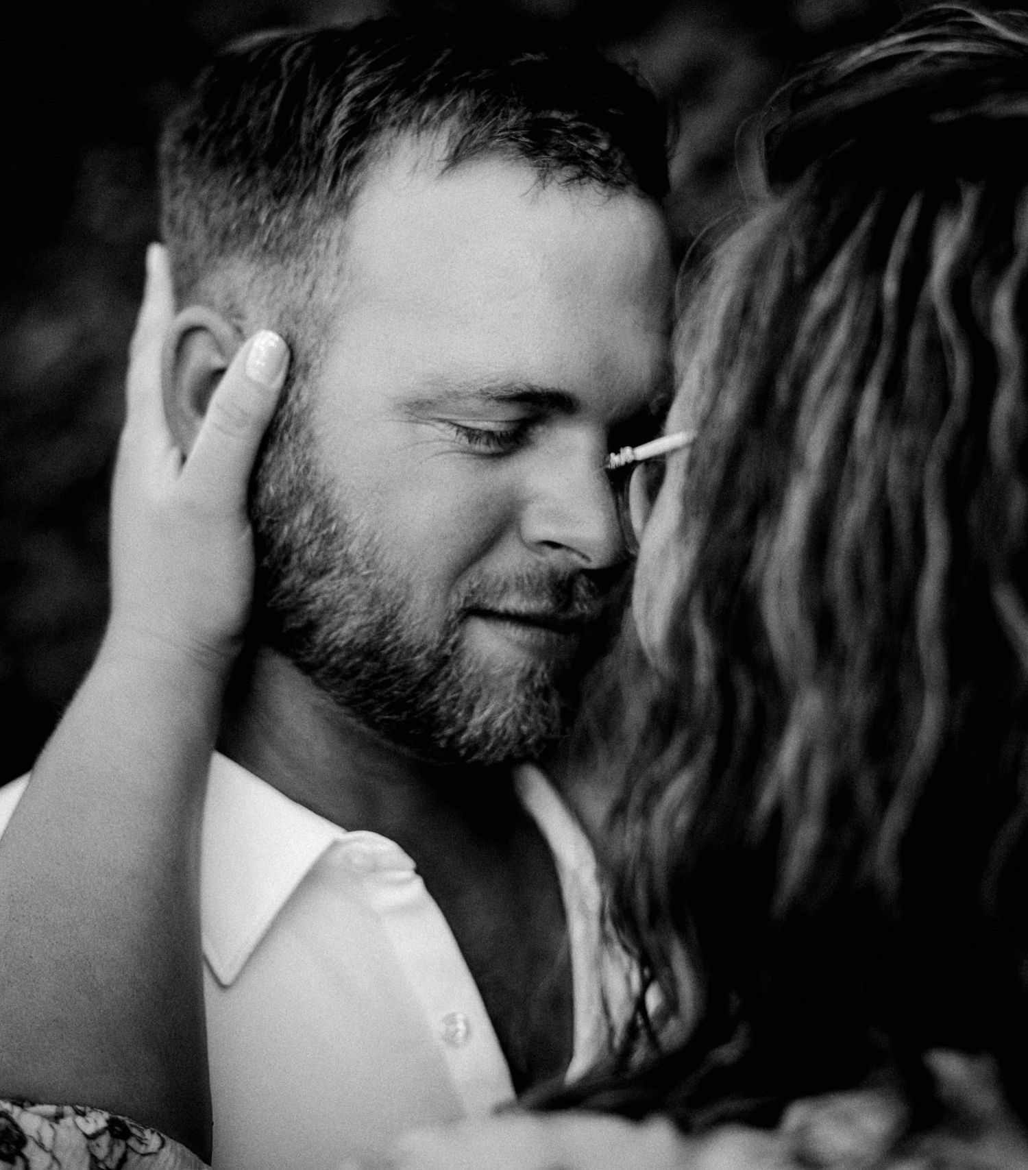 Black and white intimate photo showing tender moment with a bearded man and hand touching his face in romantic pose.