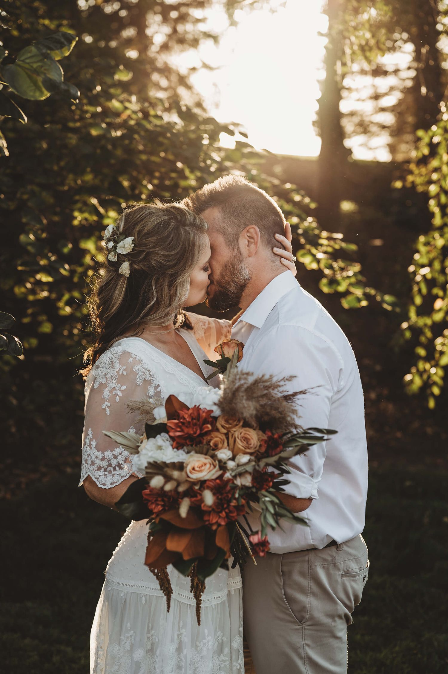 A romantic sunset moment between newlyweds with bride holding an autumn-inspired bouquet in a rustic outdoor setting.