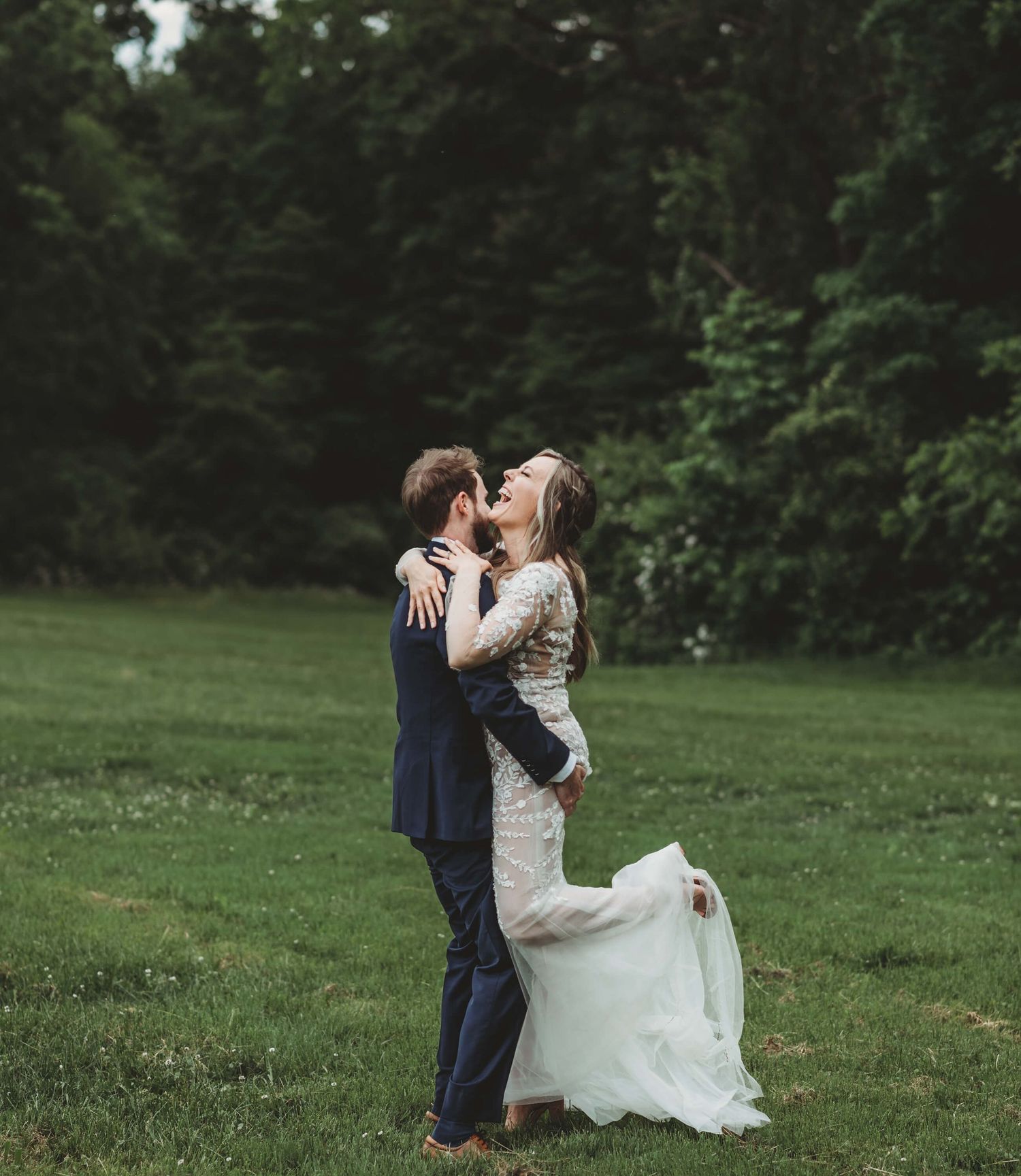Wedding couple sharing a romantic kiss on a green lawn with trees in the background.