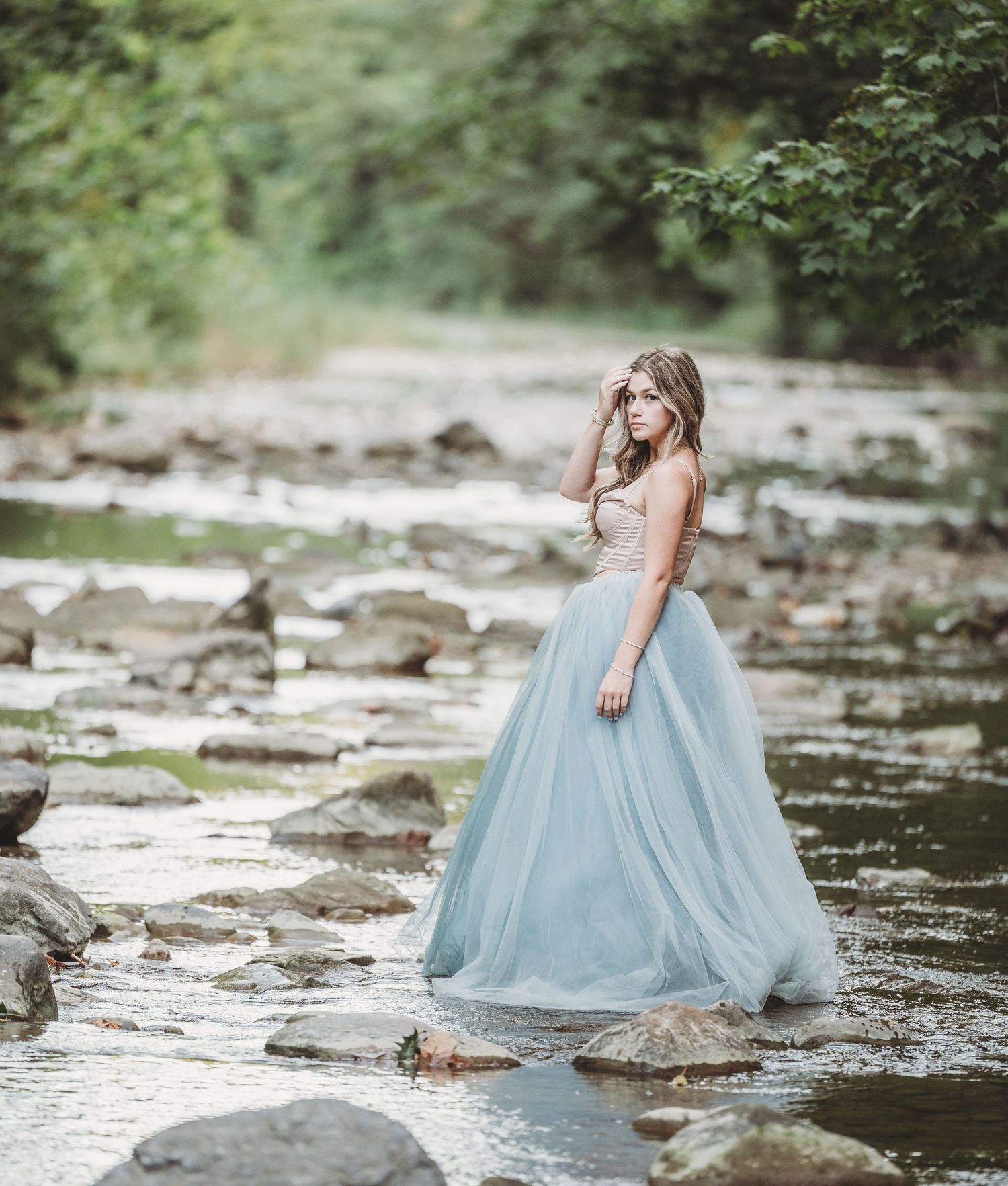 A flowing light blue tulle gown creates an ethereal scene as someone stands gracefully among rocks in a stream.