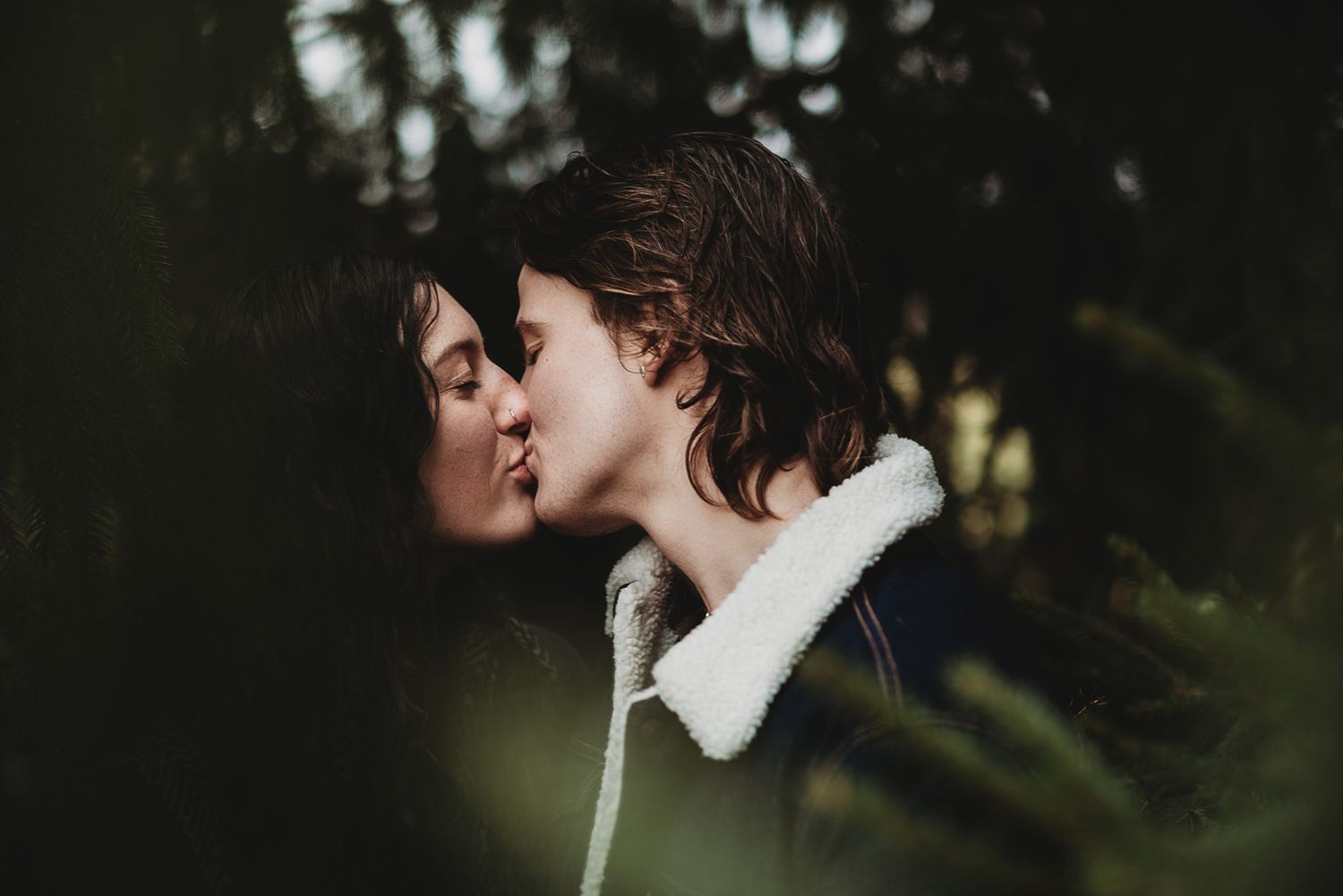 A couple shares a tender kiss during a romantic outdoor photoshoot in a lush garden setting.