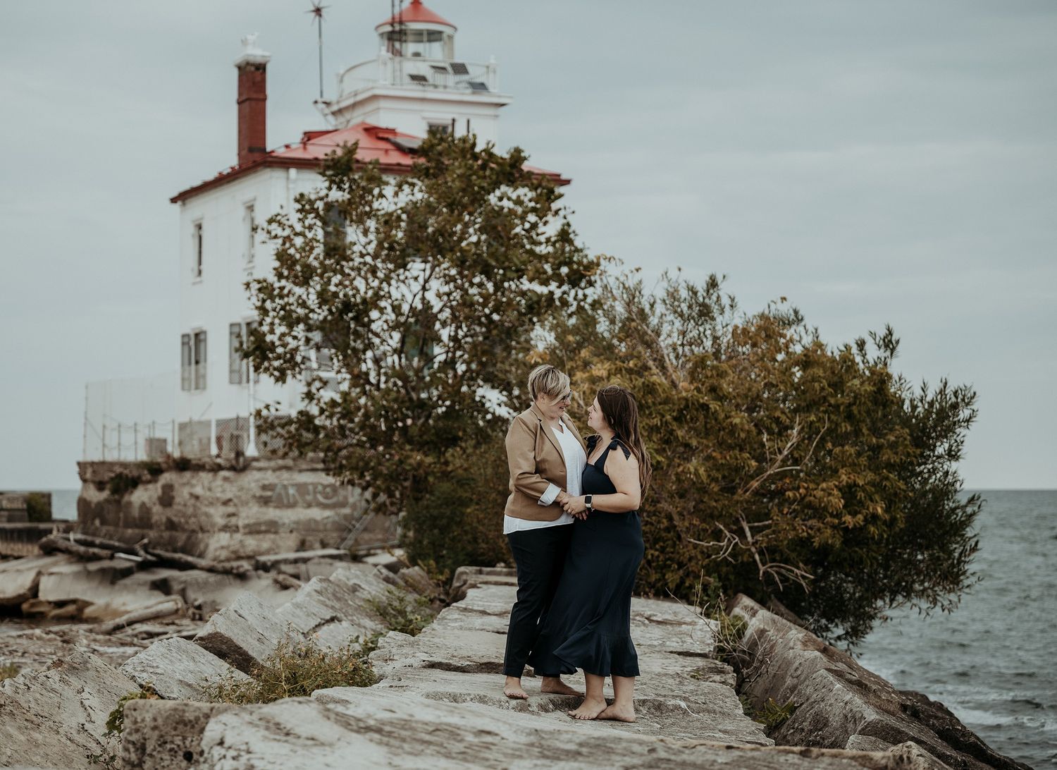 A lighthouse stands atop rocky shores with Lake Erie waters and overcast skies in the background.