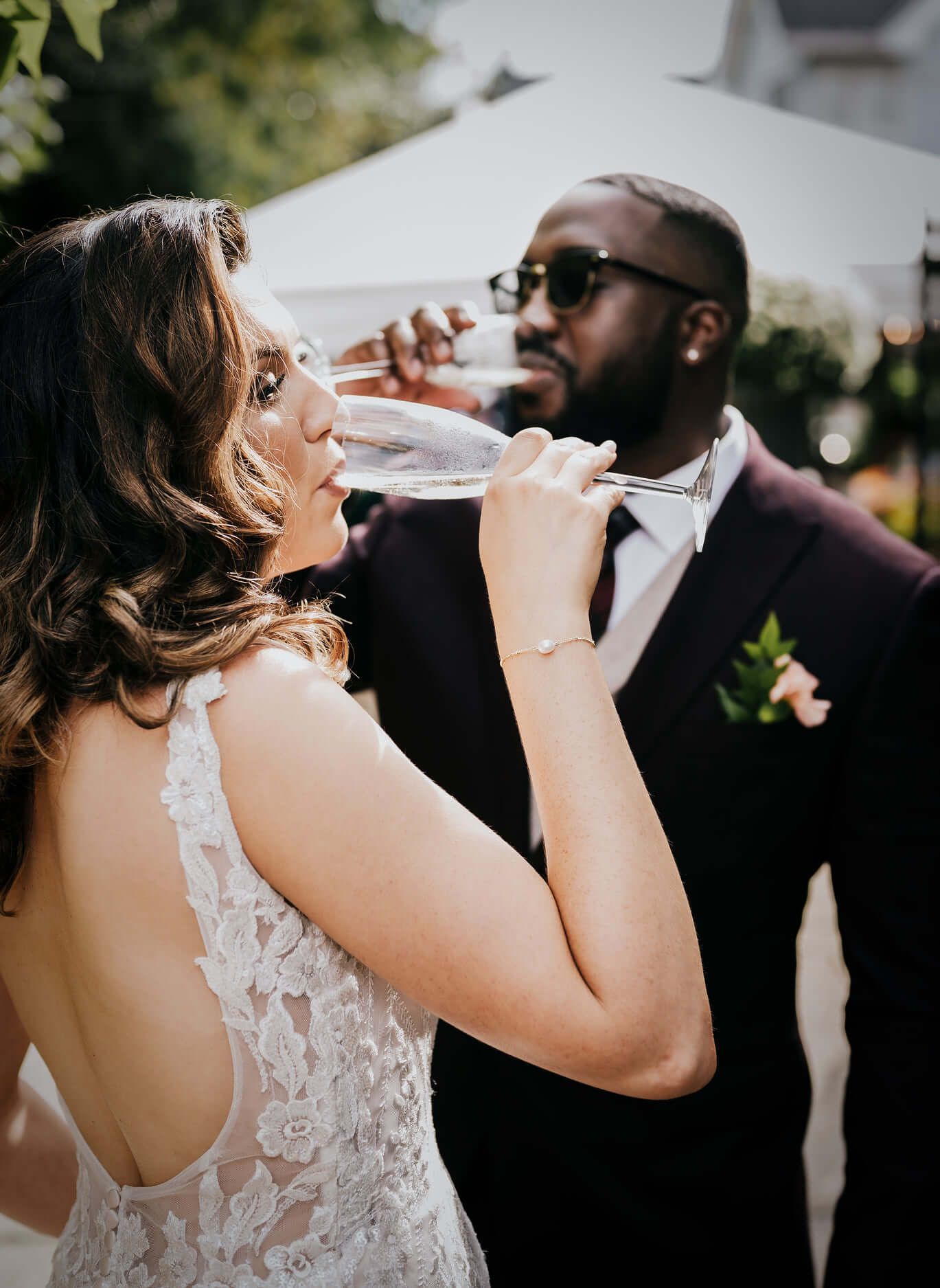Couple in wedding attire sharing champagne toast outdoors.