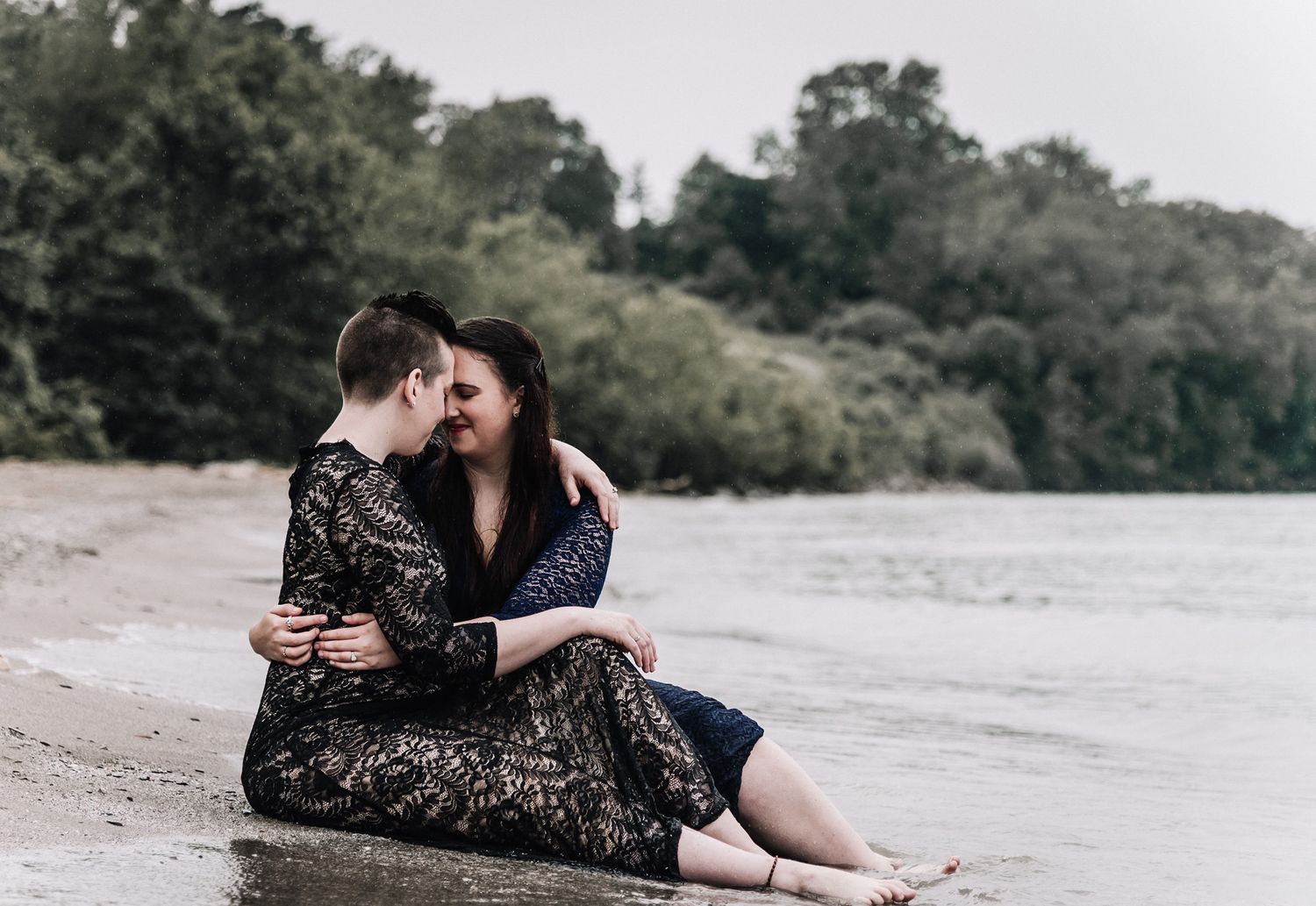 A romantic couple embraces on a riverbank during a photo session at golden hour, creating intimate outdoor portraits.