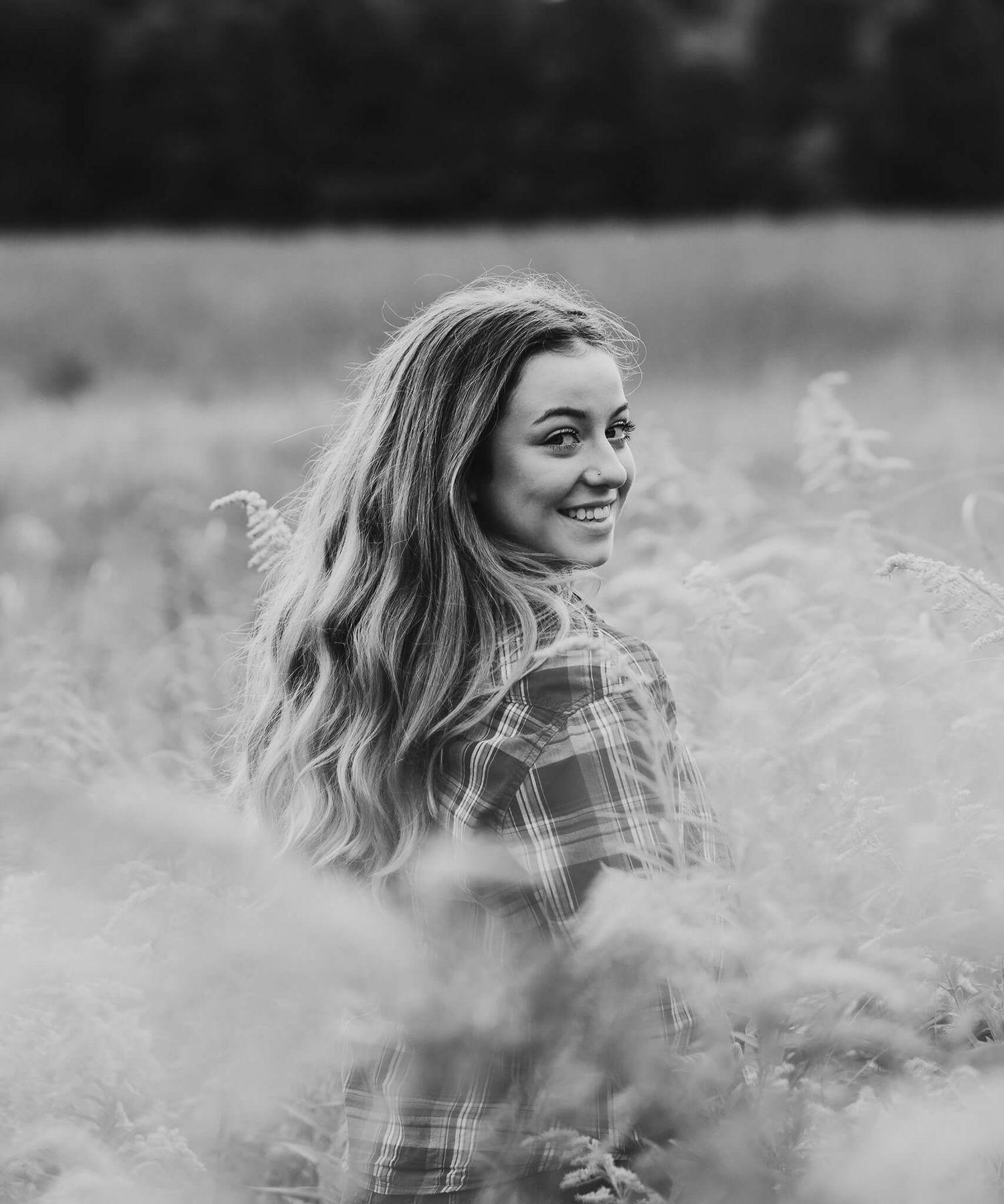 Black and white portrait of someone sitting in a field of tall grass wearing a plaid flannel shirt.