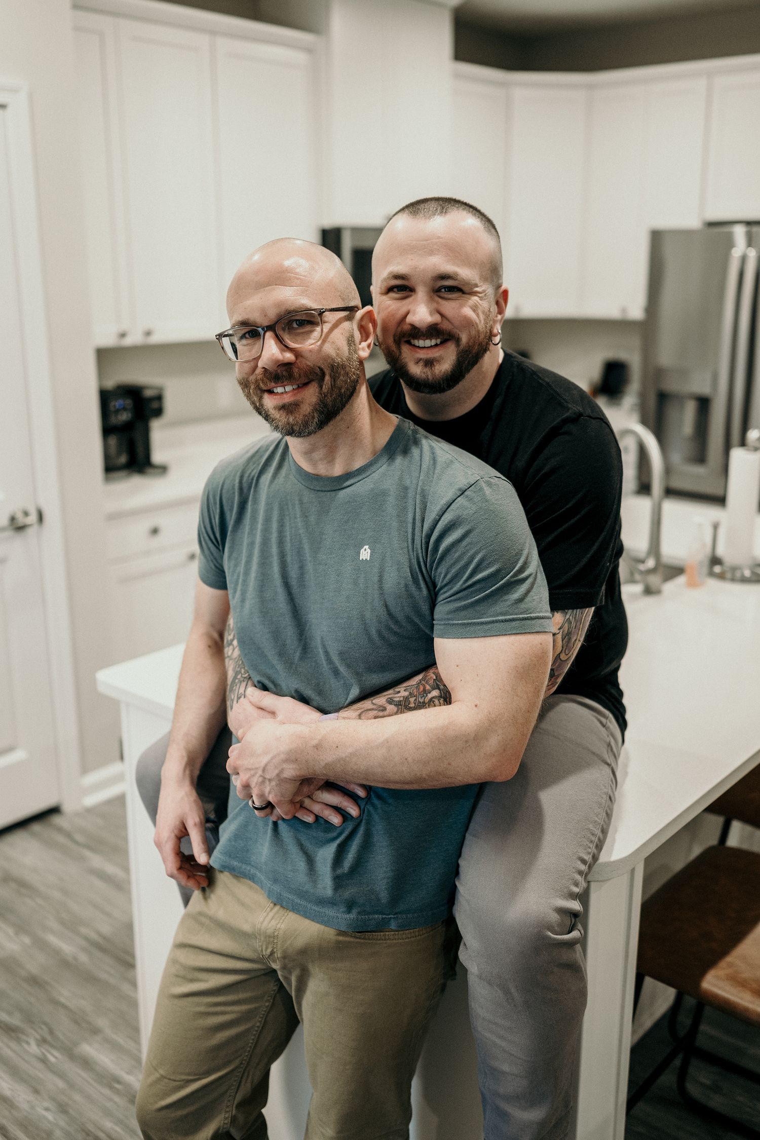 Two people sharing an intimate embrace while standing in a modern white kitchen with grey wood flooring.