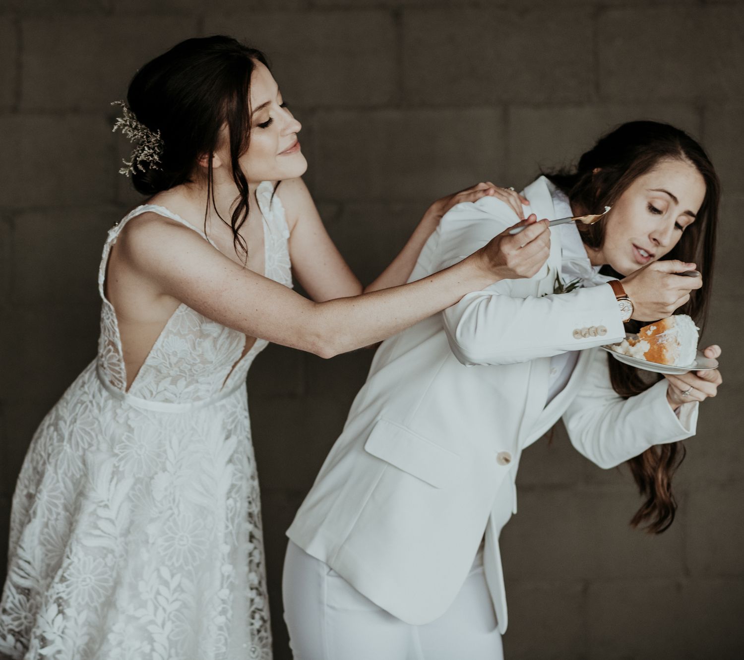 A couple in wedding attire playfully poses together with one feeding the other during a fun photo shoot moment.