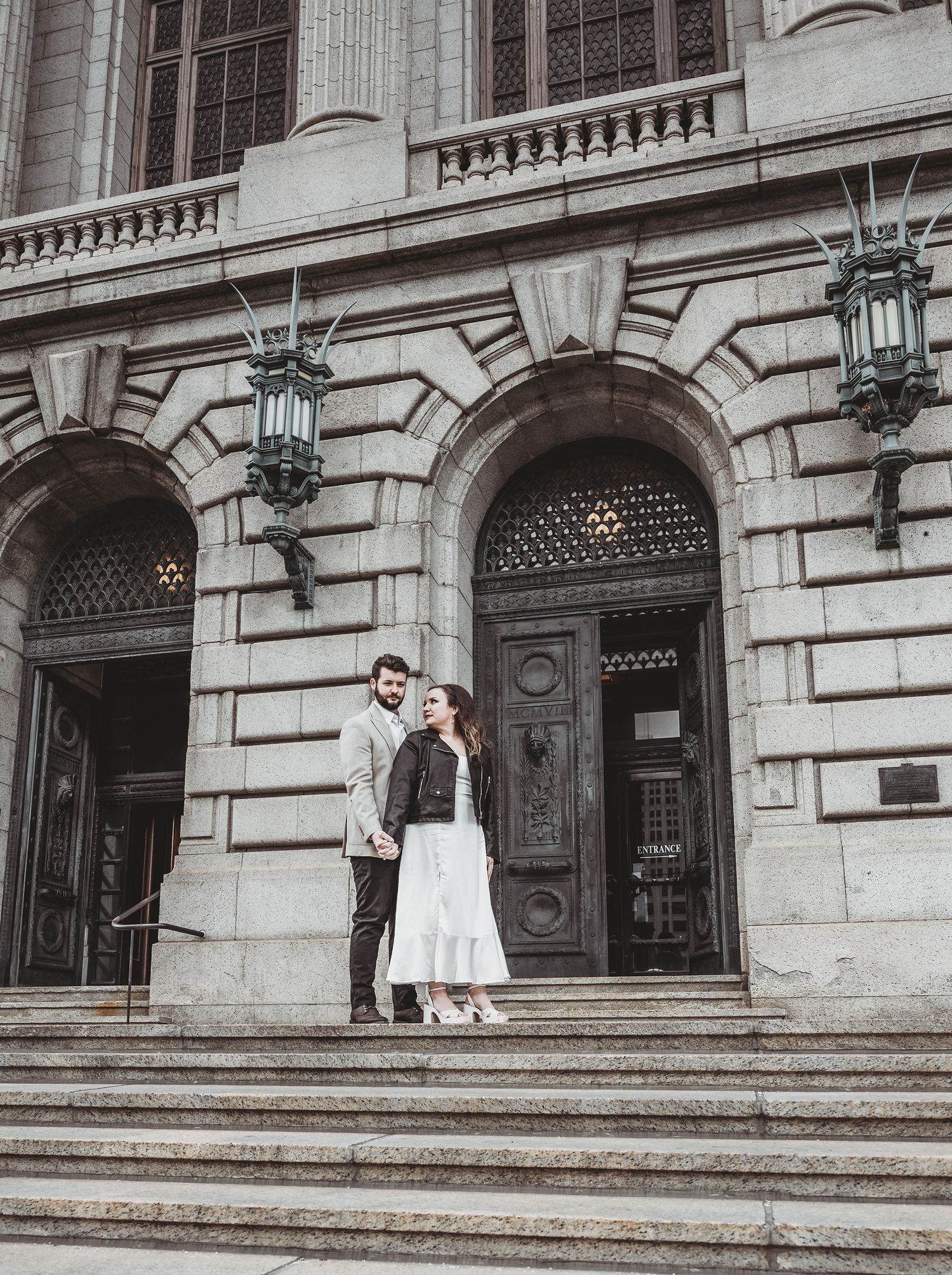 Two people standing on elegant stone steps at the entrance of a historic building with ornate architecture and lanterns.