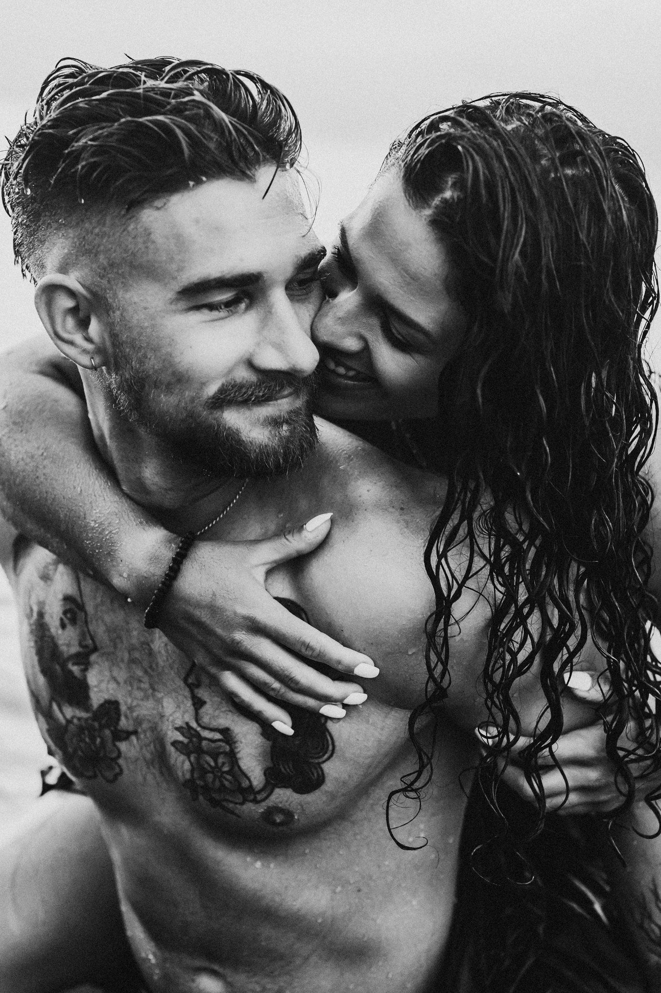 Intimate black and white portrait of couple embracing with wet hair in artistic pose.