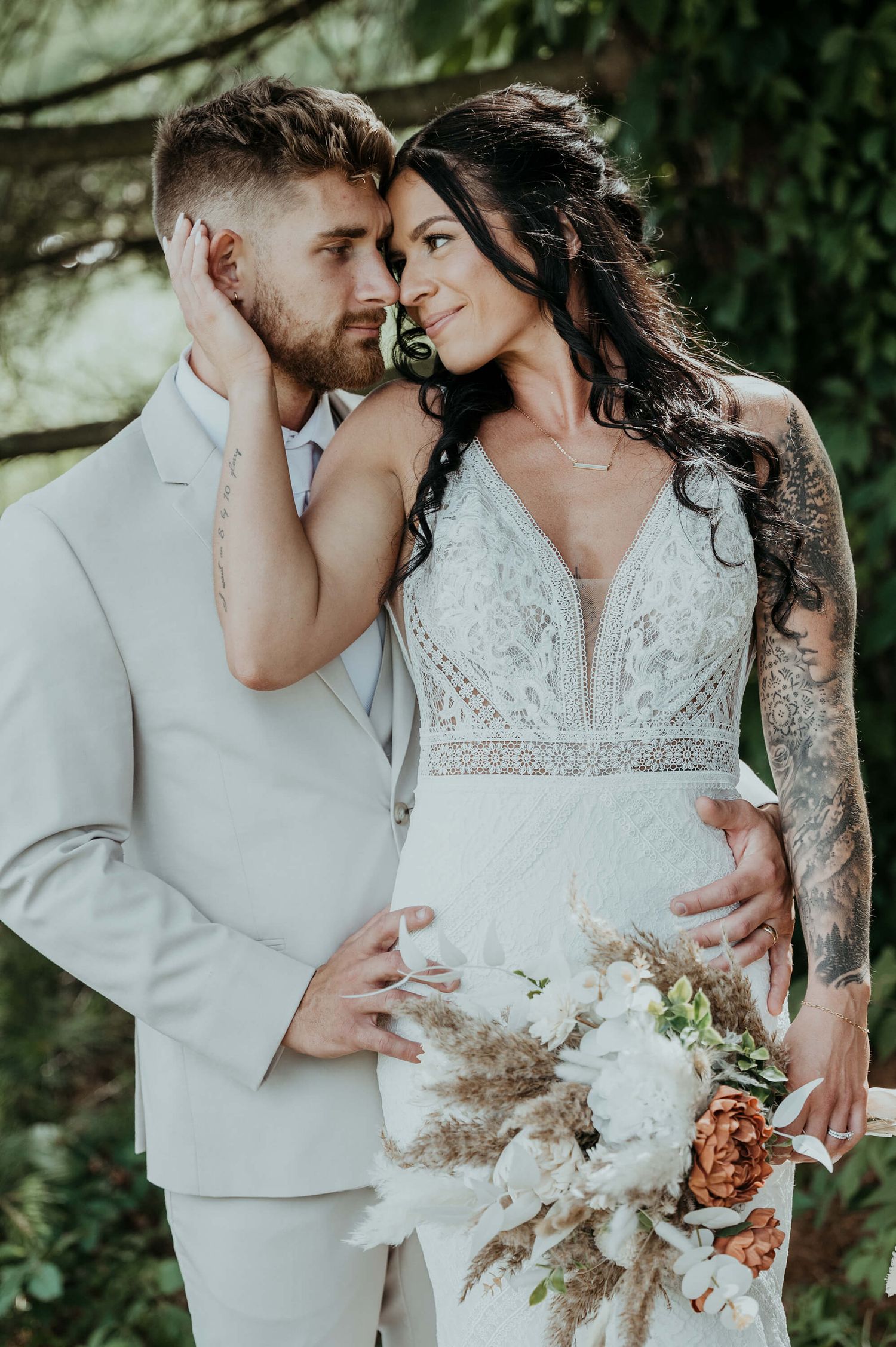 Romantic couples wedding photoshoot in white outfits against lush greenery with dried floral bouquet accents.