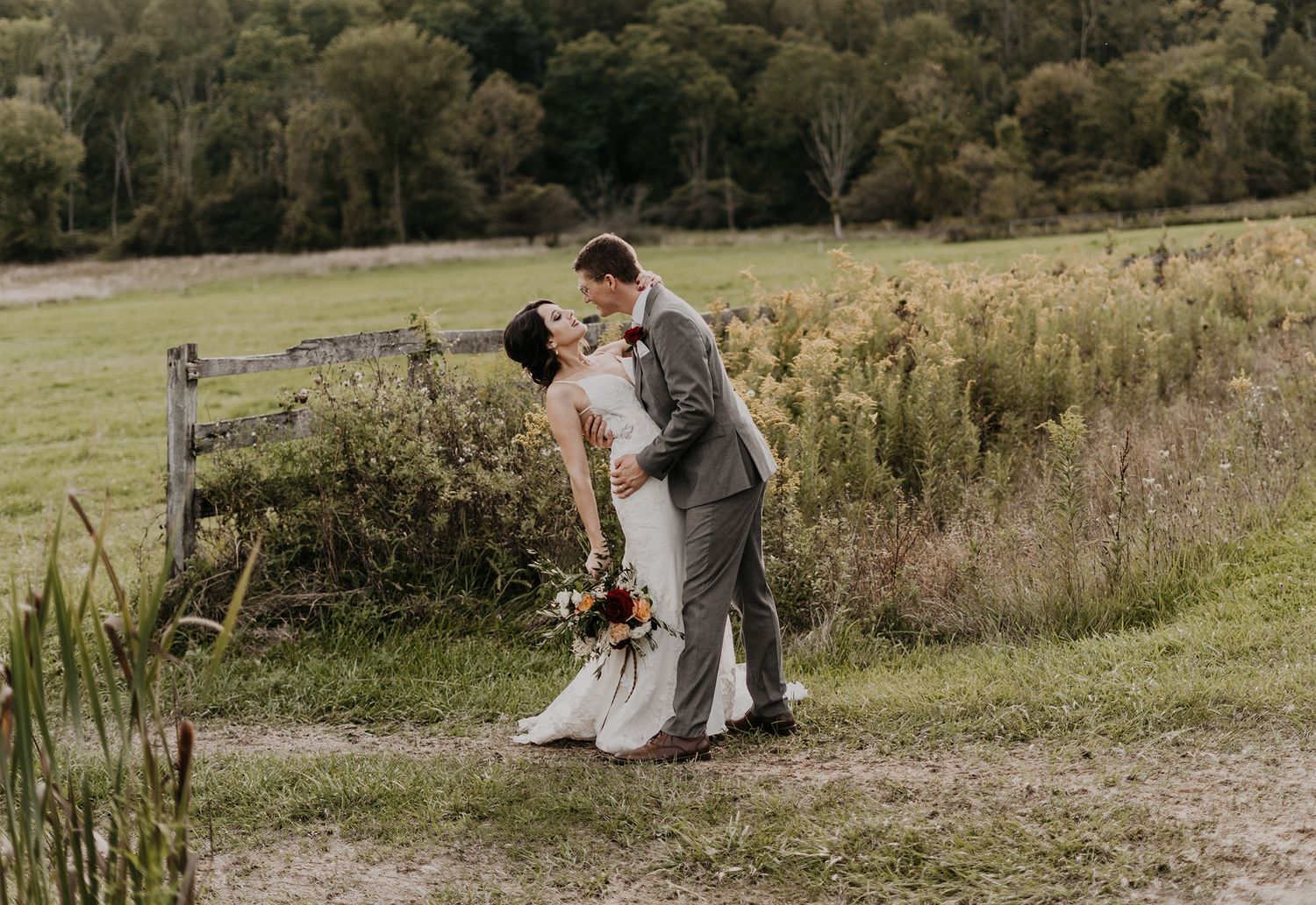 A couple shares a tender embrace in a rustic outdoor meadow setting during their wedding day photo session.