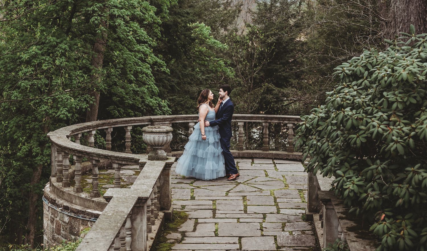 A stone pathway winds through lush gardens with ornate stone balustrades and steps in a romantic garden setting.
