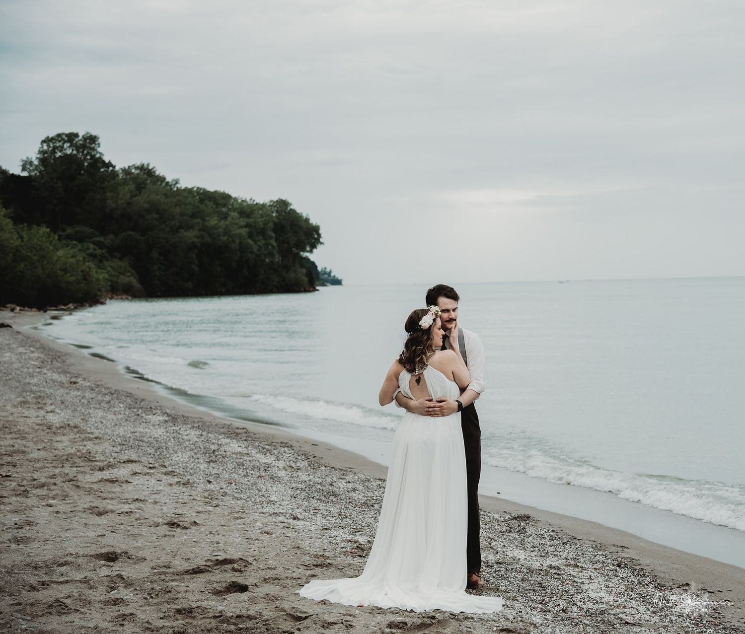A romantic beach wedding photoshoot with a couple embracing on a rocky shoreline with moody overcast skies.