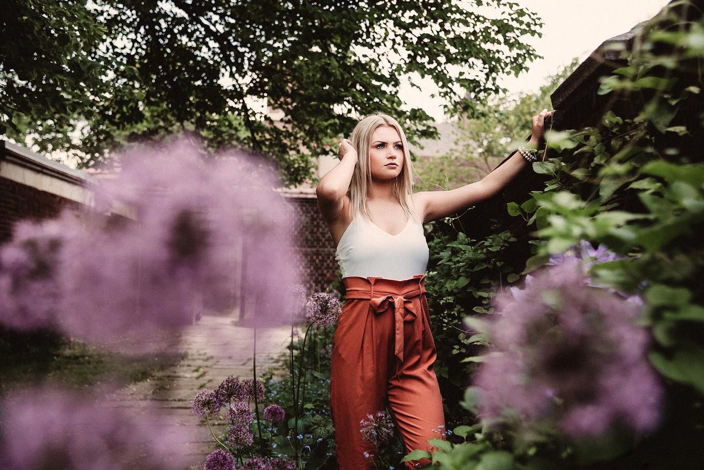 Artistic portrait with purple smoke effects in garden setting featuring rustic fashion and natural foliage.