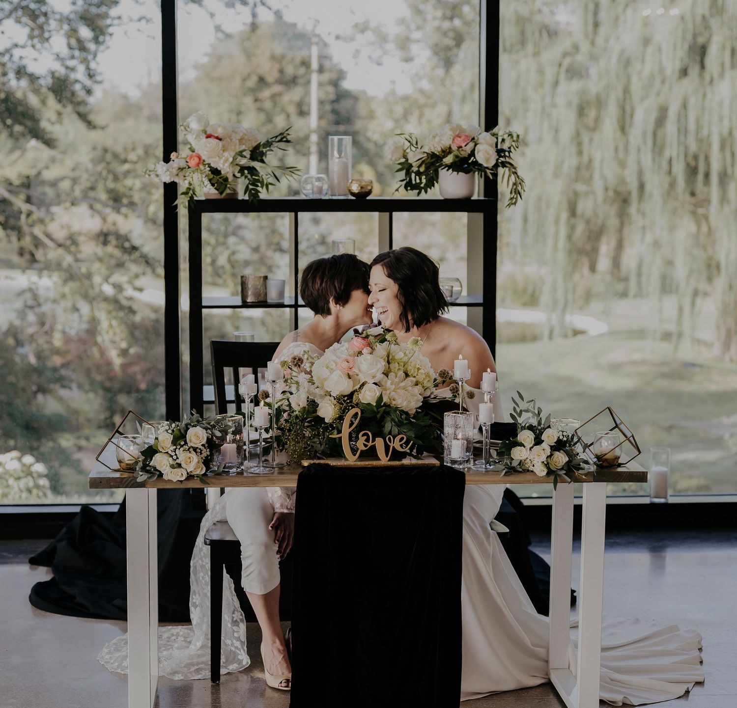 Romantic wedding table setting with black backdrop and soft floral arrangements in blush and white tones.