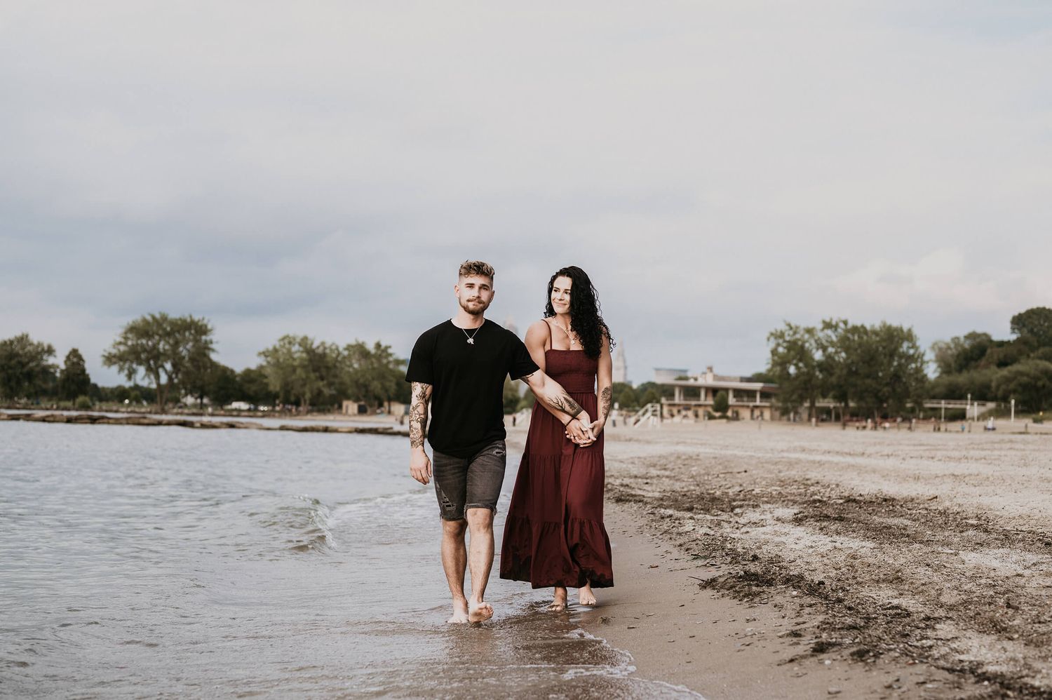Couple walking barefoot along the water's edge at a beach during a cloudy day.