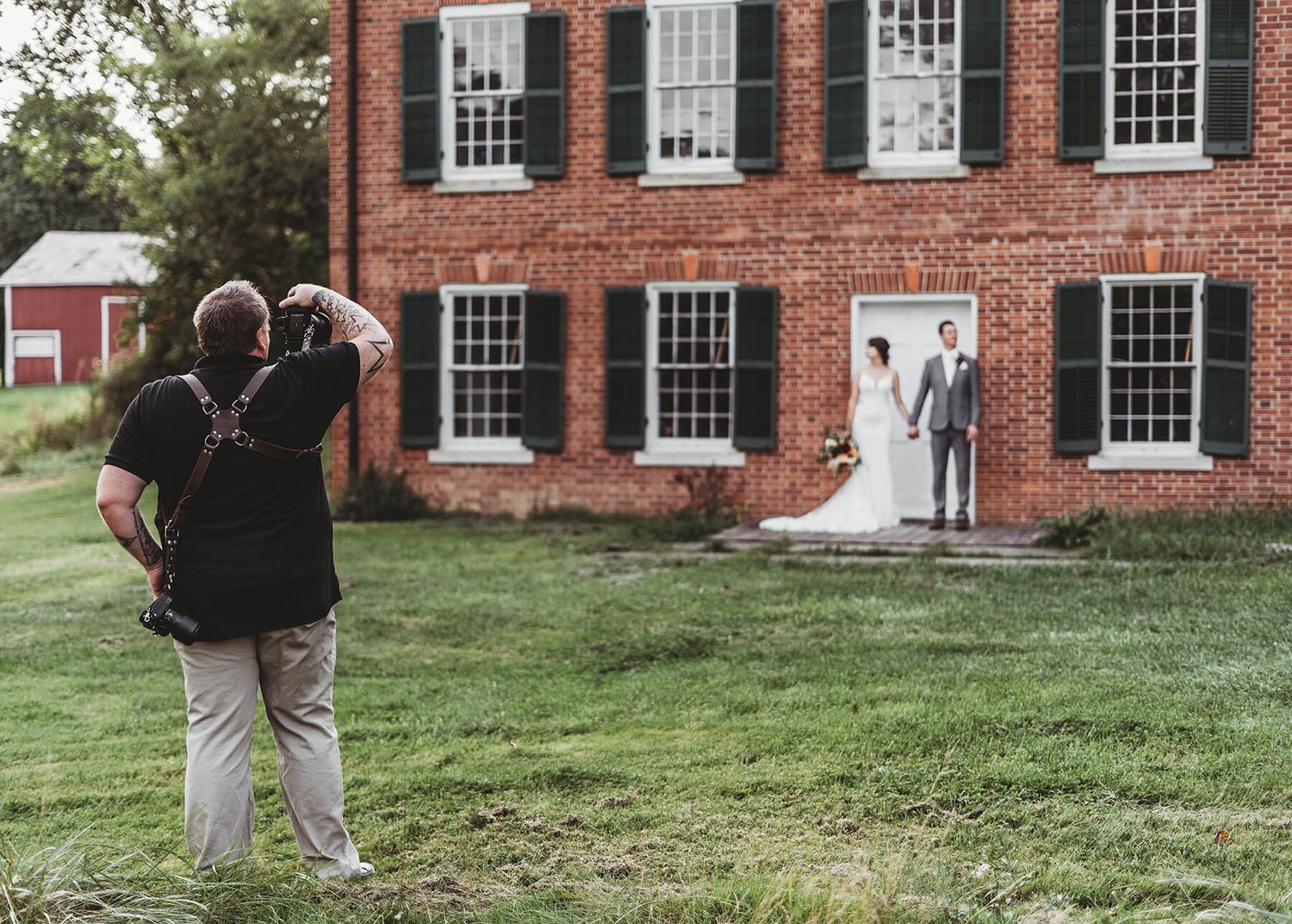 A photographer captures a couple's wedding portrait in front of a historic red brick colonial building with white windows.