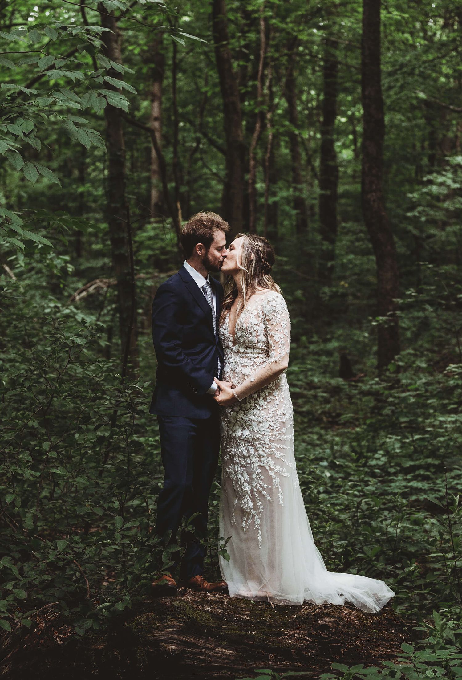 A romantic couple shares intimate moments against a lush forest backdrop in an outdoor wedding setting.