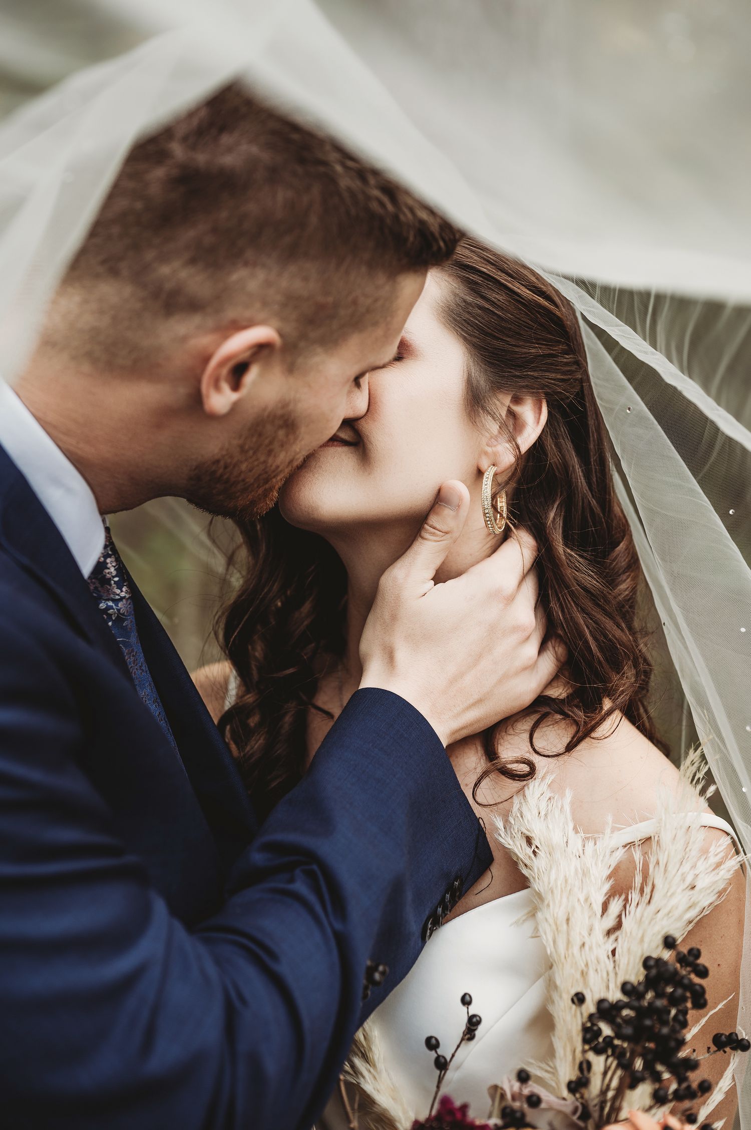 Wedding close-up of couple in a romantic kiss, with bride wearing a lace white dress and groom in navy suit.