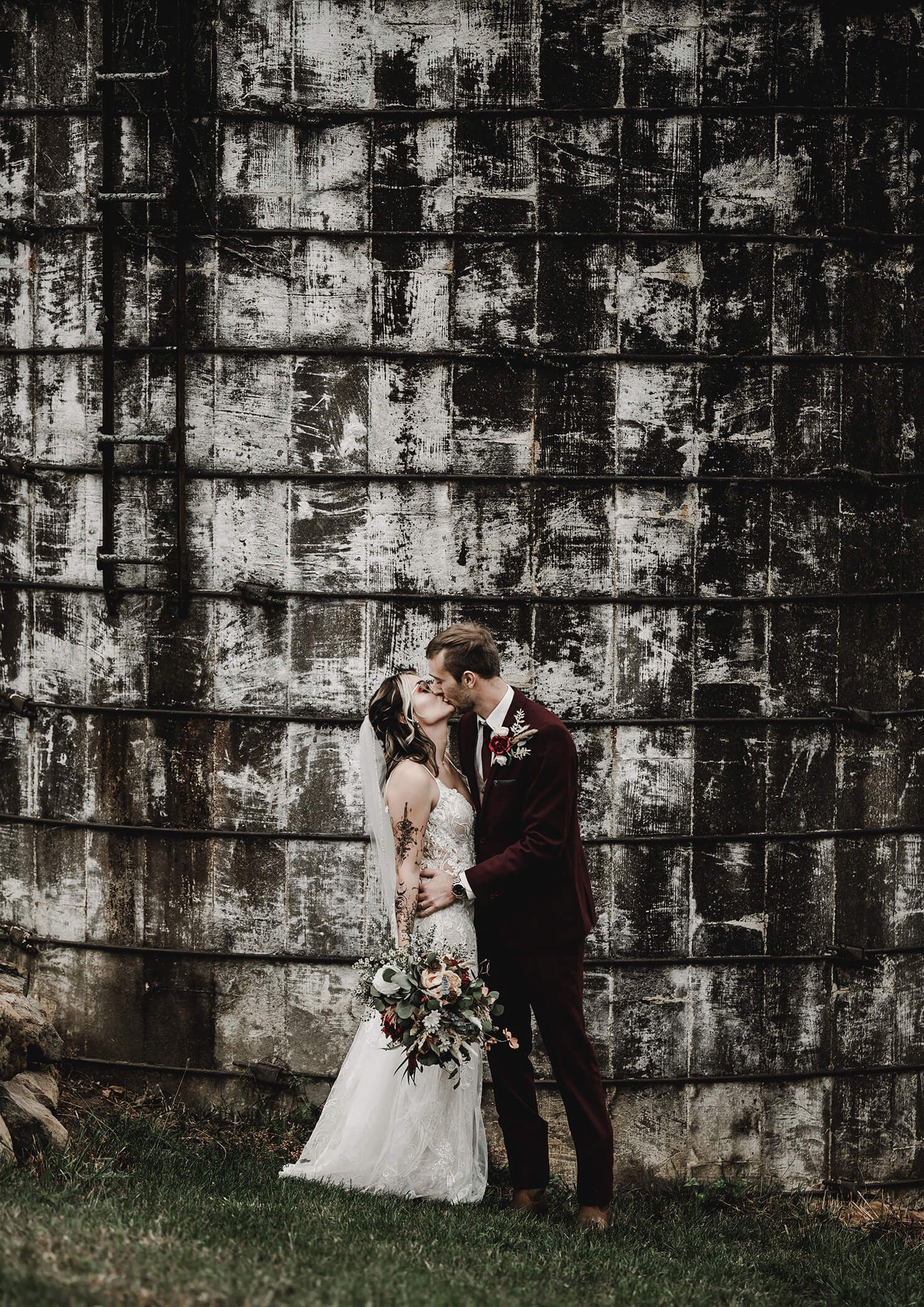 Romantic wedding couple sharing an intimate moment against a weathered concrete wall outdoors.