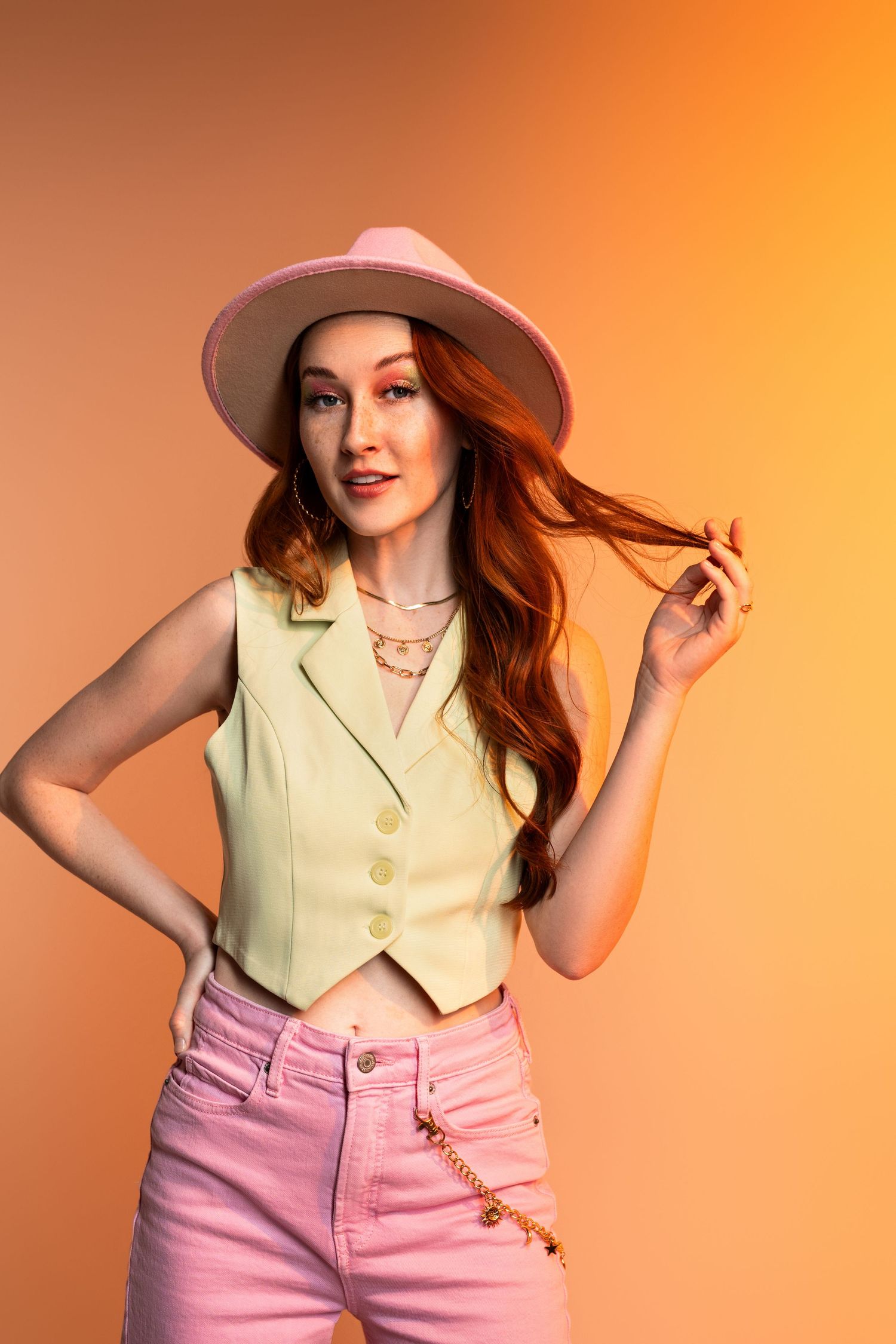 Fashion model poses in vintage-inspired yellow top and pink high-waisted pants against orange background.
