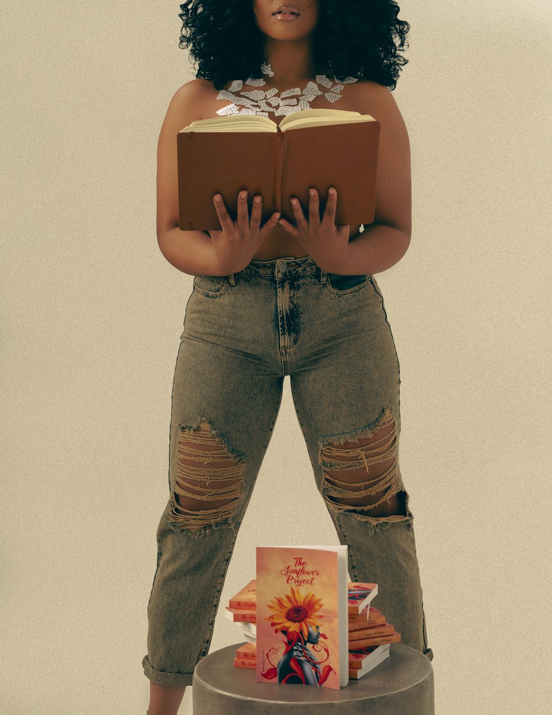 Person in distressed jeans holding colorful art book against beige wall.