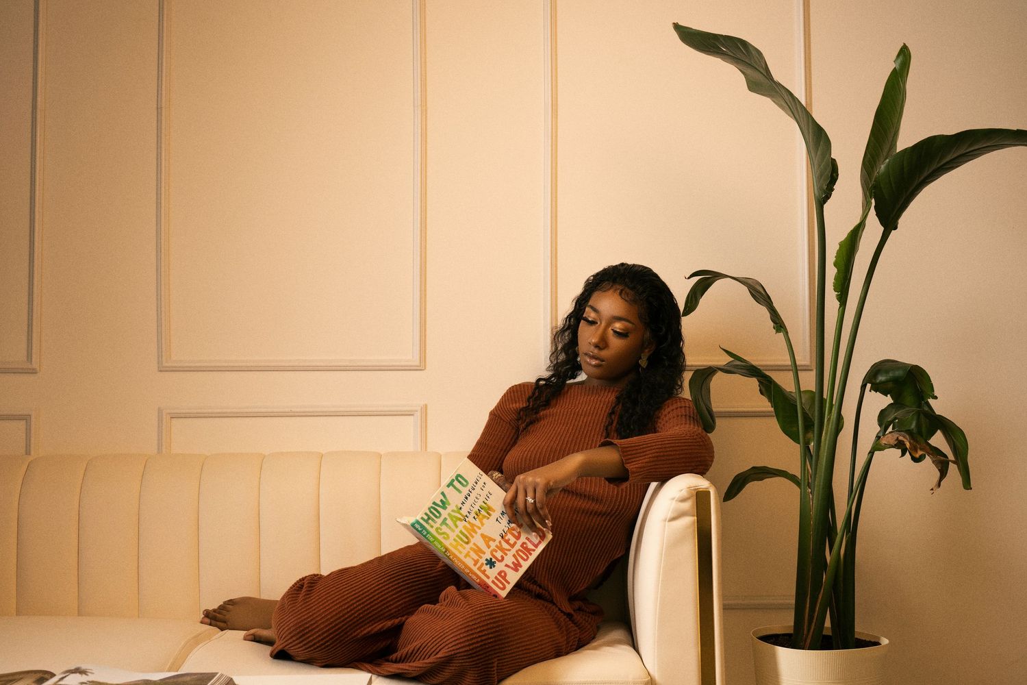 Cozy reading scene with brown cushions and indoor plants in warm lighting.