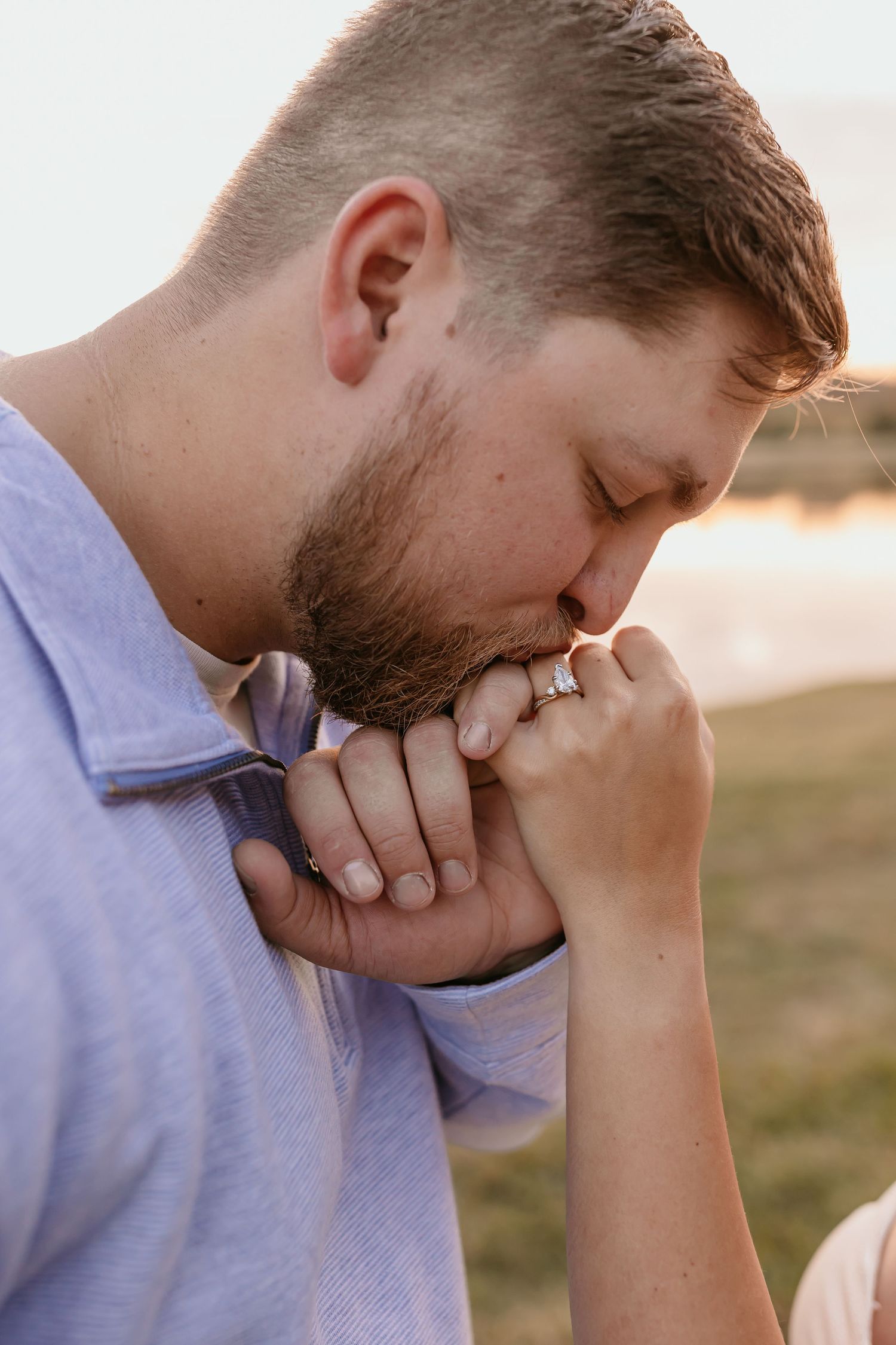 Person in light blue shirt kissing clasped hands in intimate prayer or reflection during golden hour.
