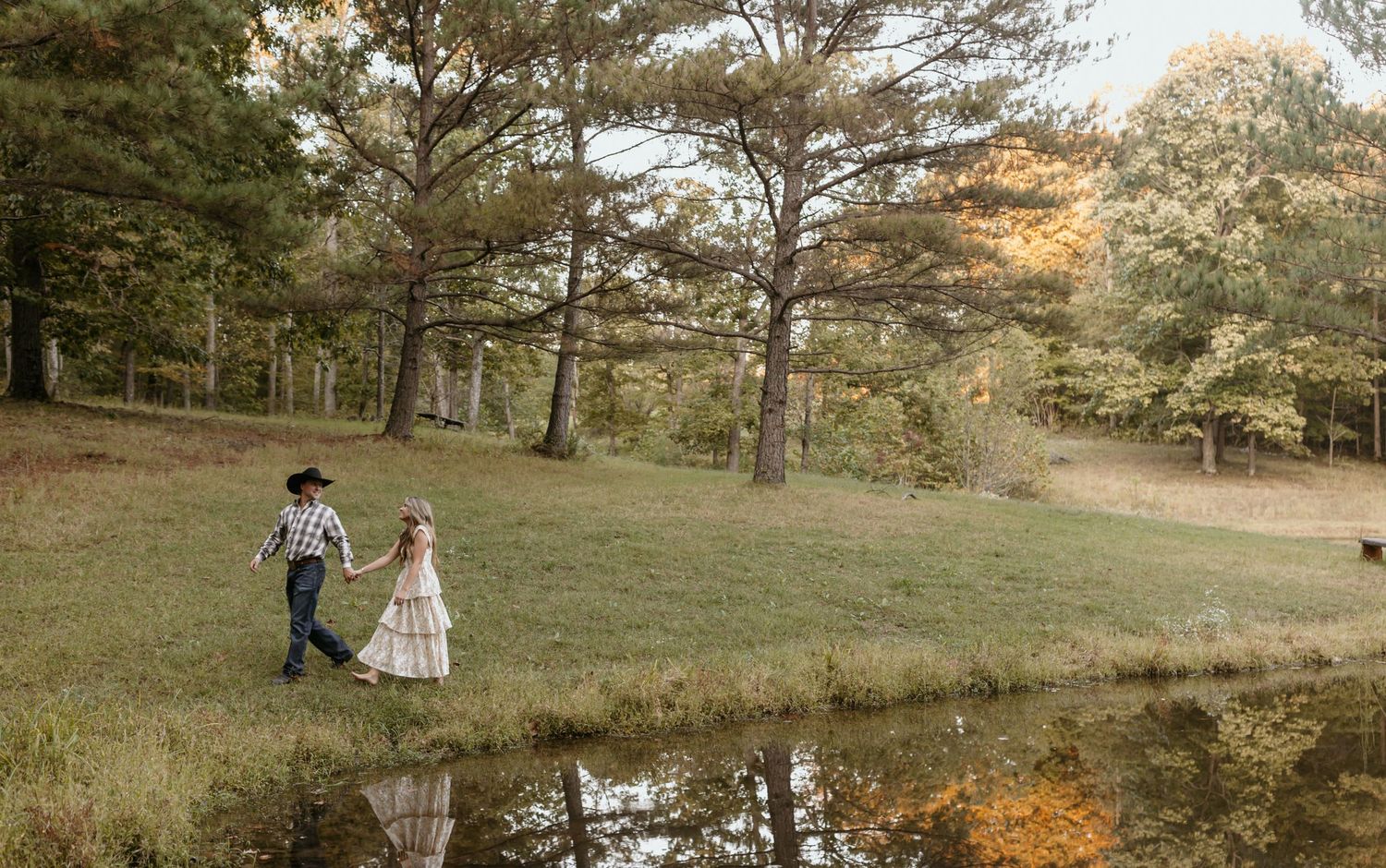 Two small figures walking near a reflective pond with autumn trees in the background.