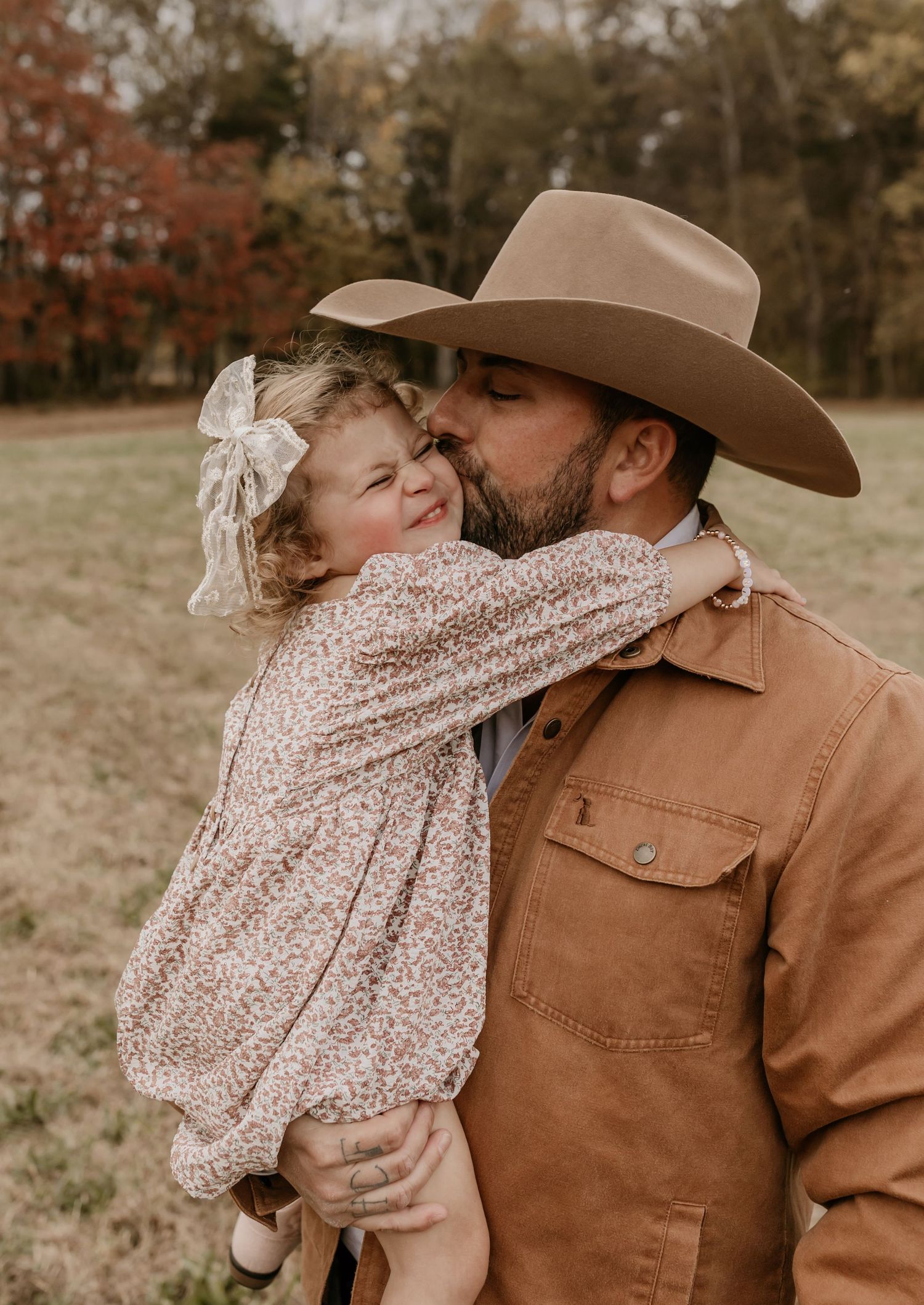 Tender moment captured in autumn field wearing western attire.