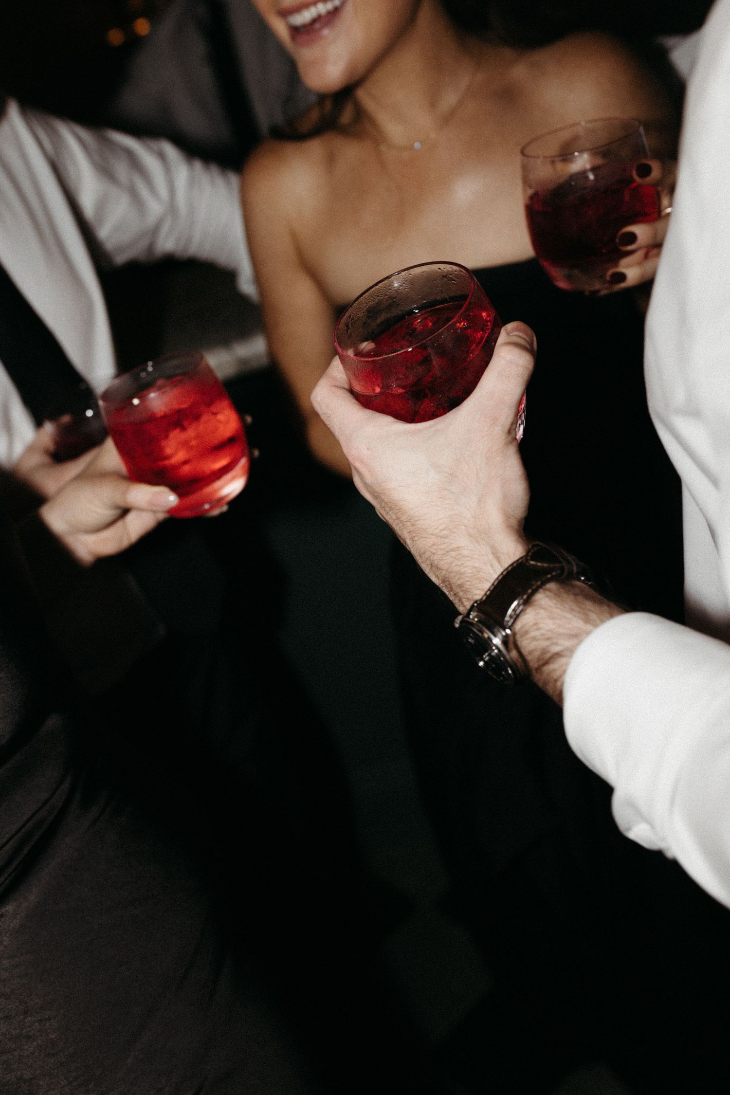 A sequence of hands holding and toasting with wine glasses filled with red wine against a dark background.