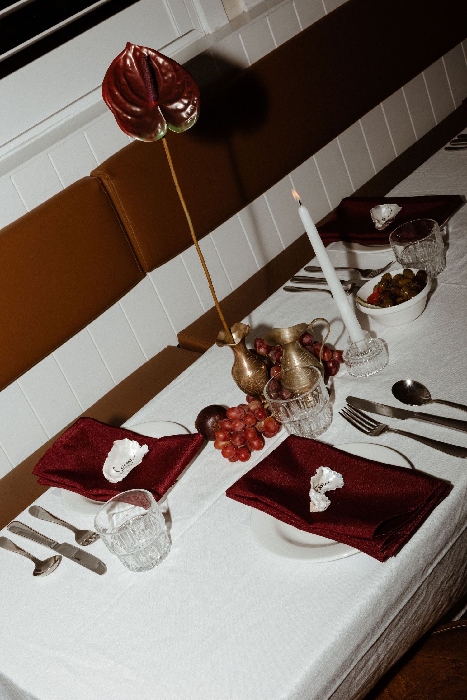 Elegant table setting with red napkins, crystal glasses, white candle and anthurium flower on crisp white tablecloth.