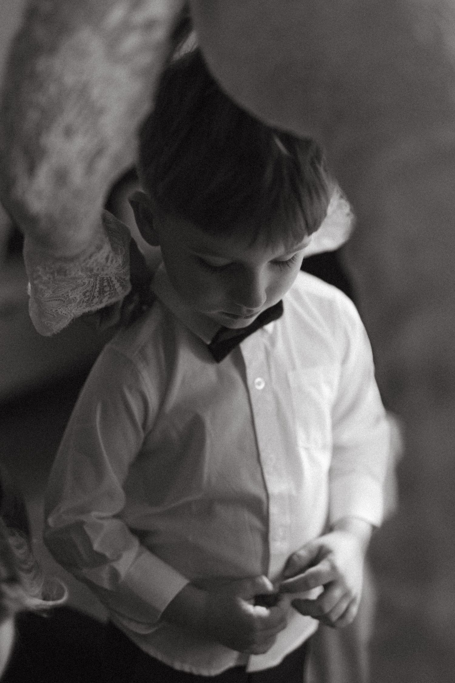 Black and white photograph showing a figure in a white button-down shirt looking down while standing in dim lighting.