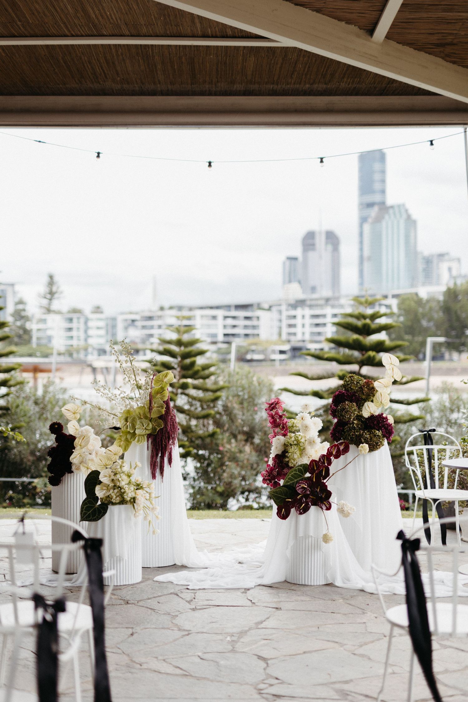 Wedding ceremony setup with white floral arrangements on pedestals against an urban skyline backdrop.