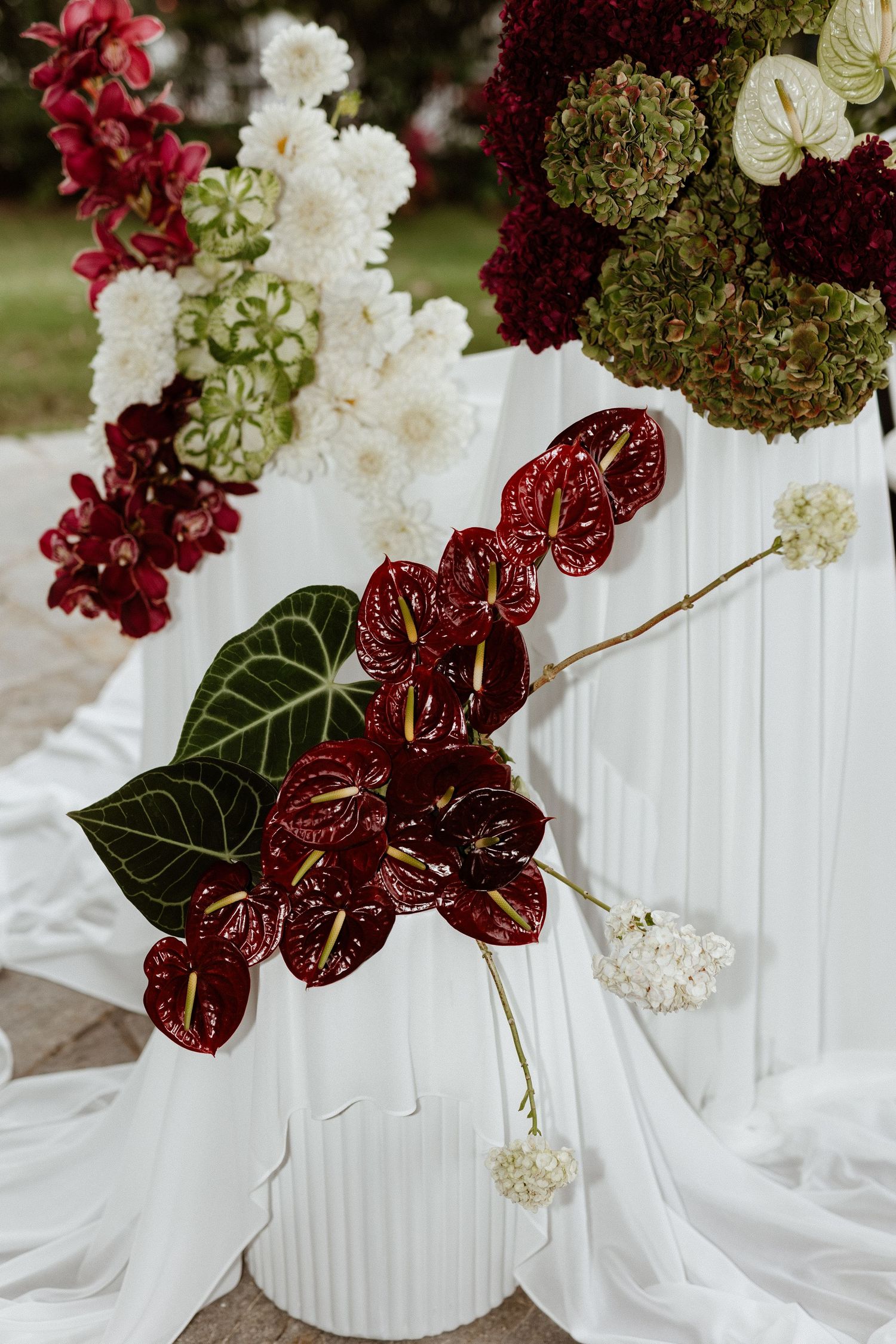 Modern white floral arrangements with burgundy anthurium flowers and white hydrangeas in ribbed ceramic vases.