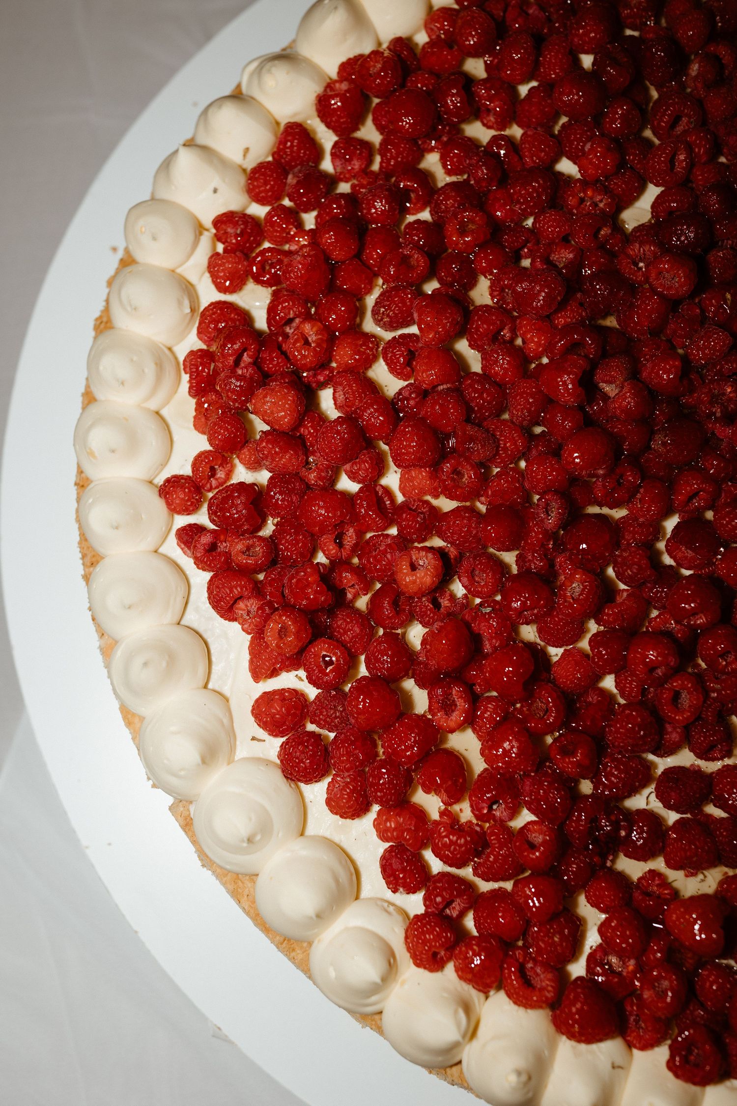 A beautiful wedding cake decorated with fresh red raspberries and white cream piping around the edge.